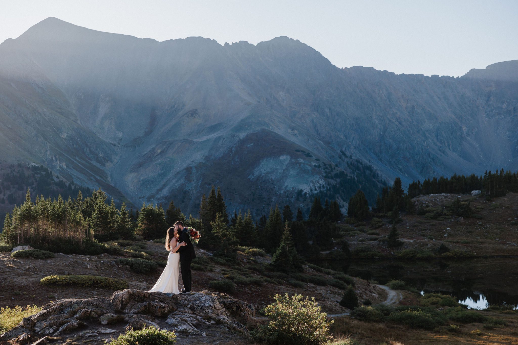 bride and groom pose on rock during their mountain lake wedding in colorado