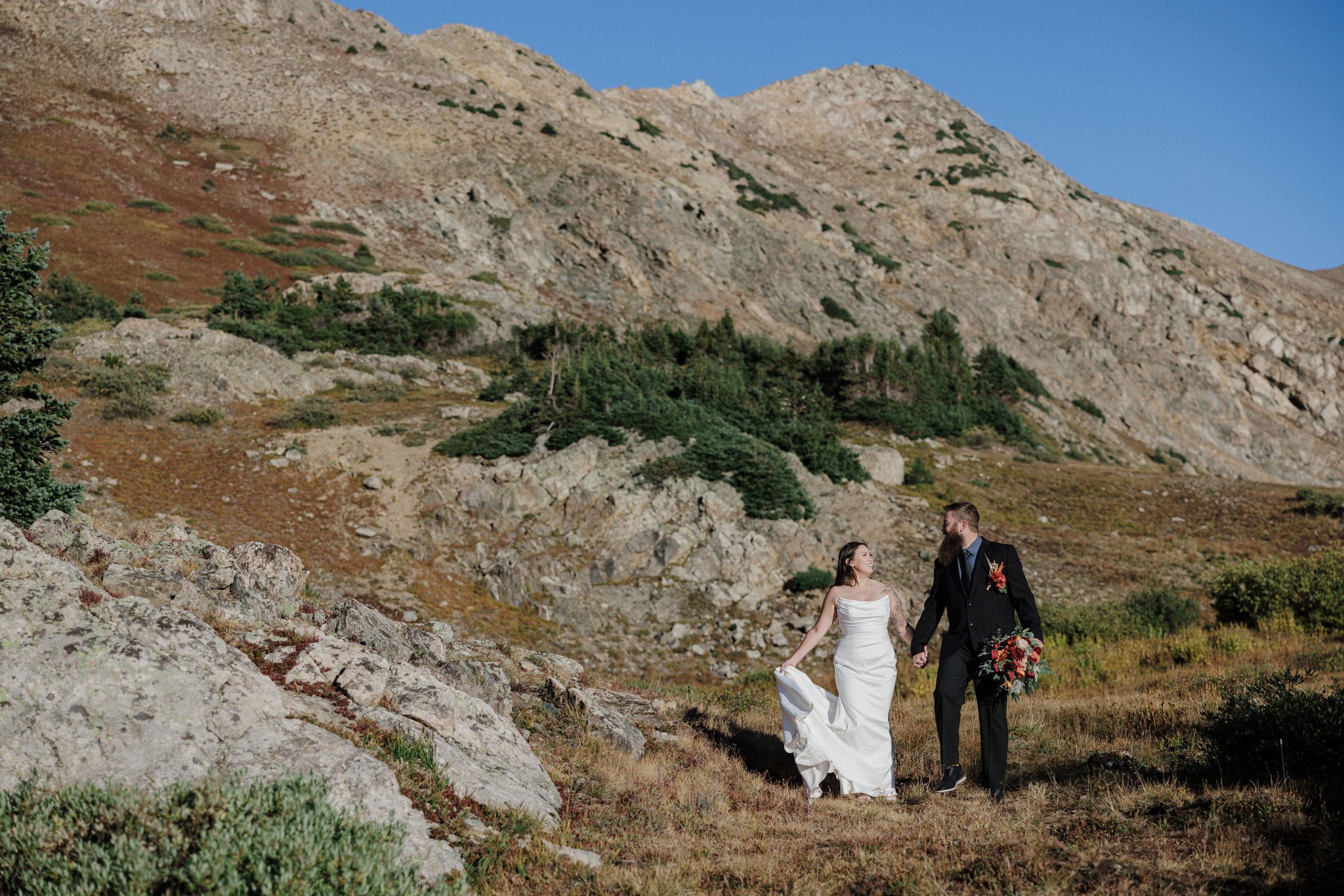 bride and groom hold hands and walk through mountains in colorado during fall