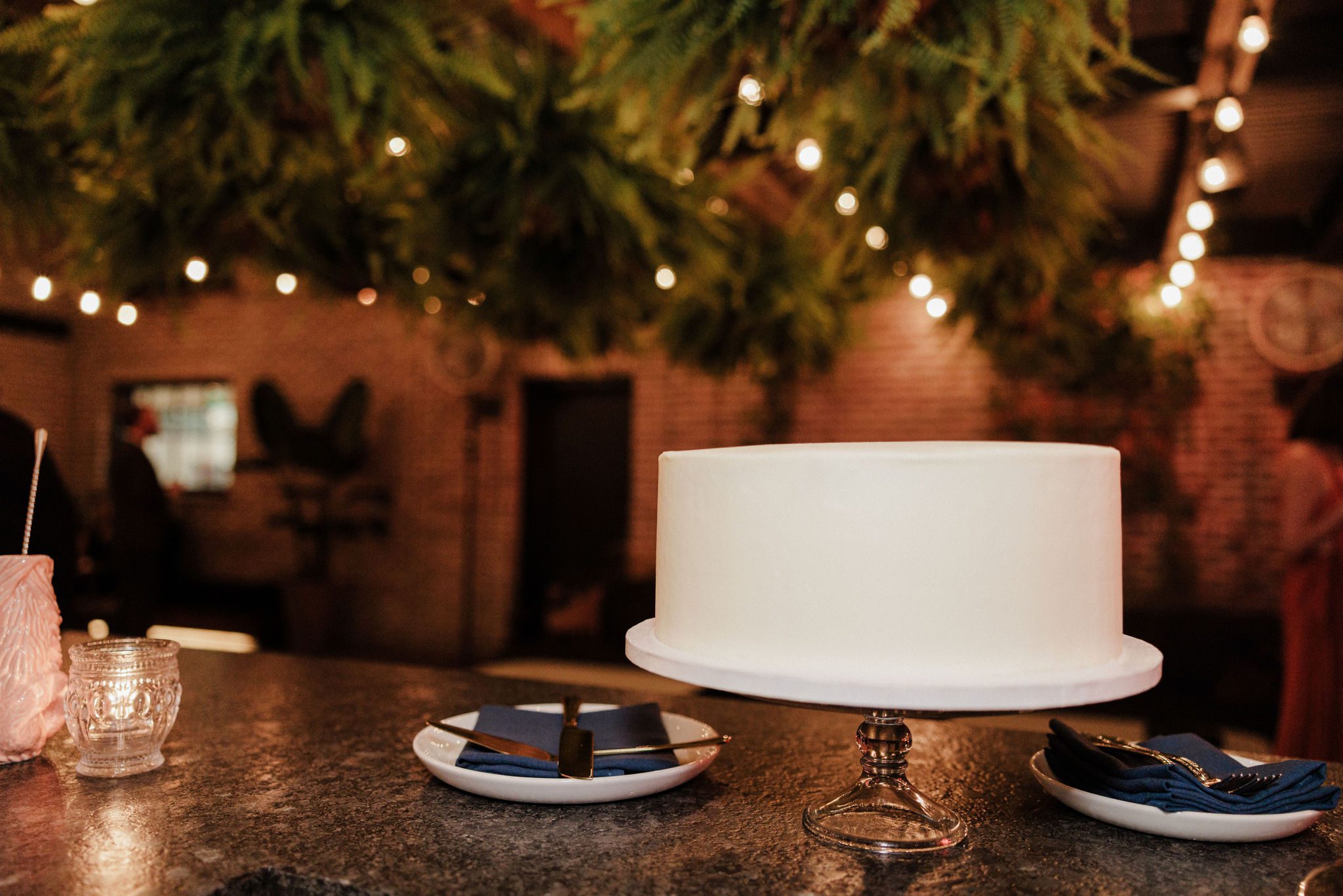 cake sits on a bartop with ferns hanging from the ceiling of wedding venue rooftop terrace 