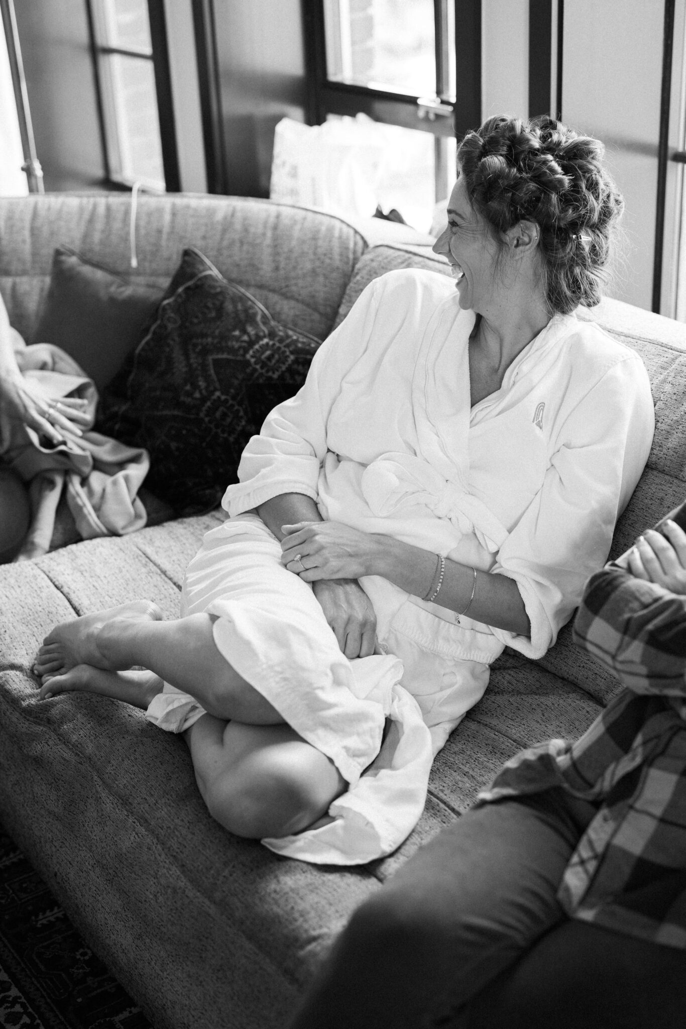 bride sits on couch and laughs during hair and make up at the ramble hotel, a denver micro wedding venue