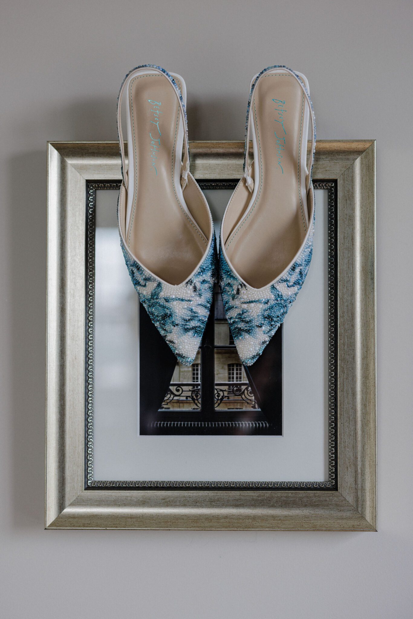 blue wedding shoes hang from photo frame on wall