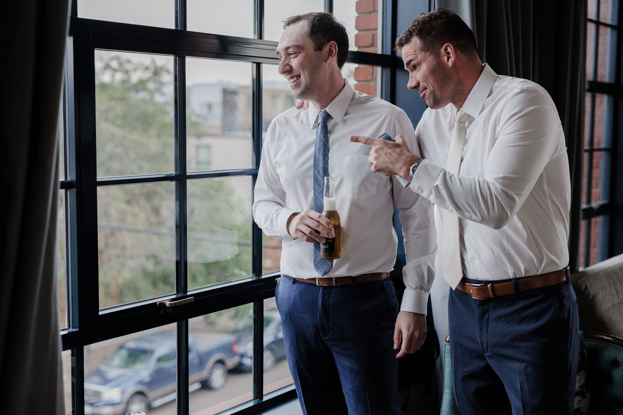 groomsmen drink beer and stand by window at suite in the denver micro wedding wedding venue, the ramble hotel