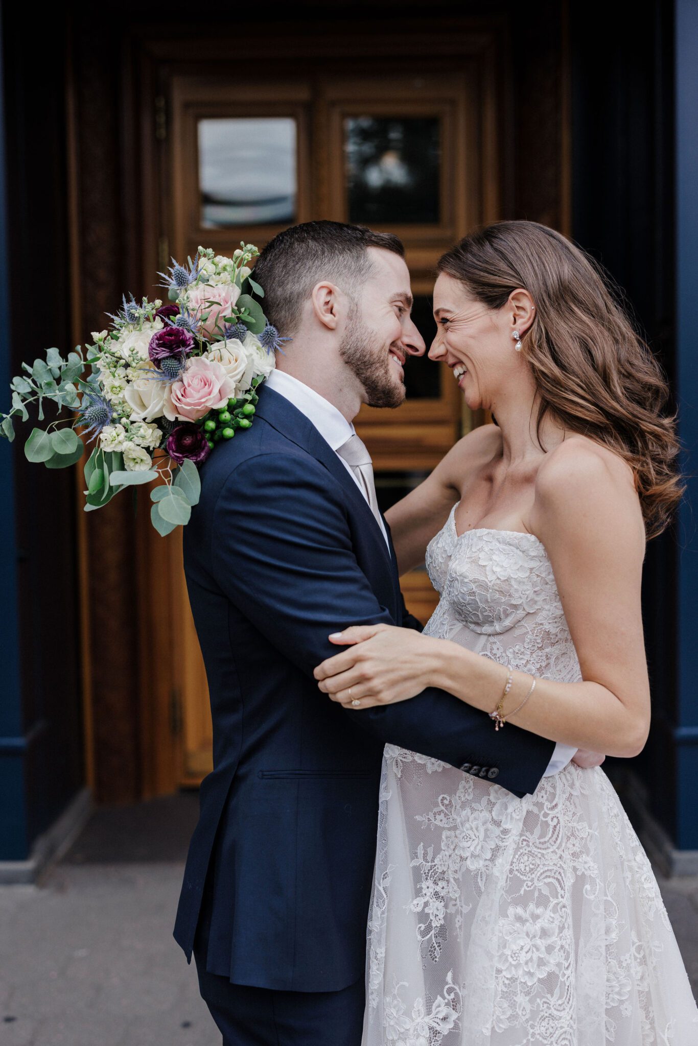 bride and groom smile and embrace while taking photos in front of the ramble hotel in denver