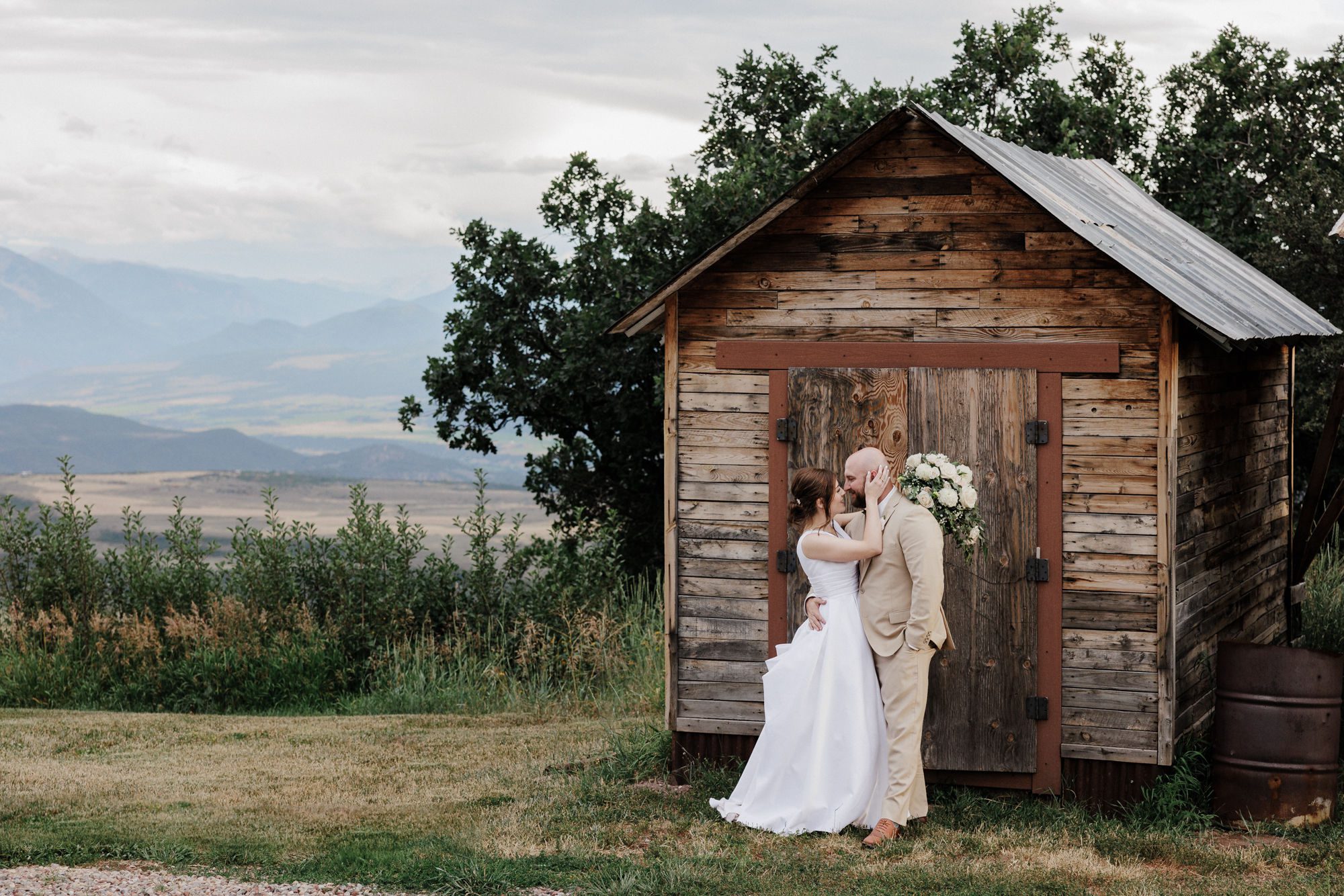 bride and groom kiss beside shed during wedding photos in late summer