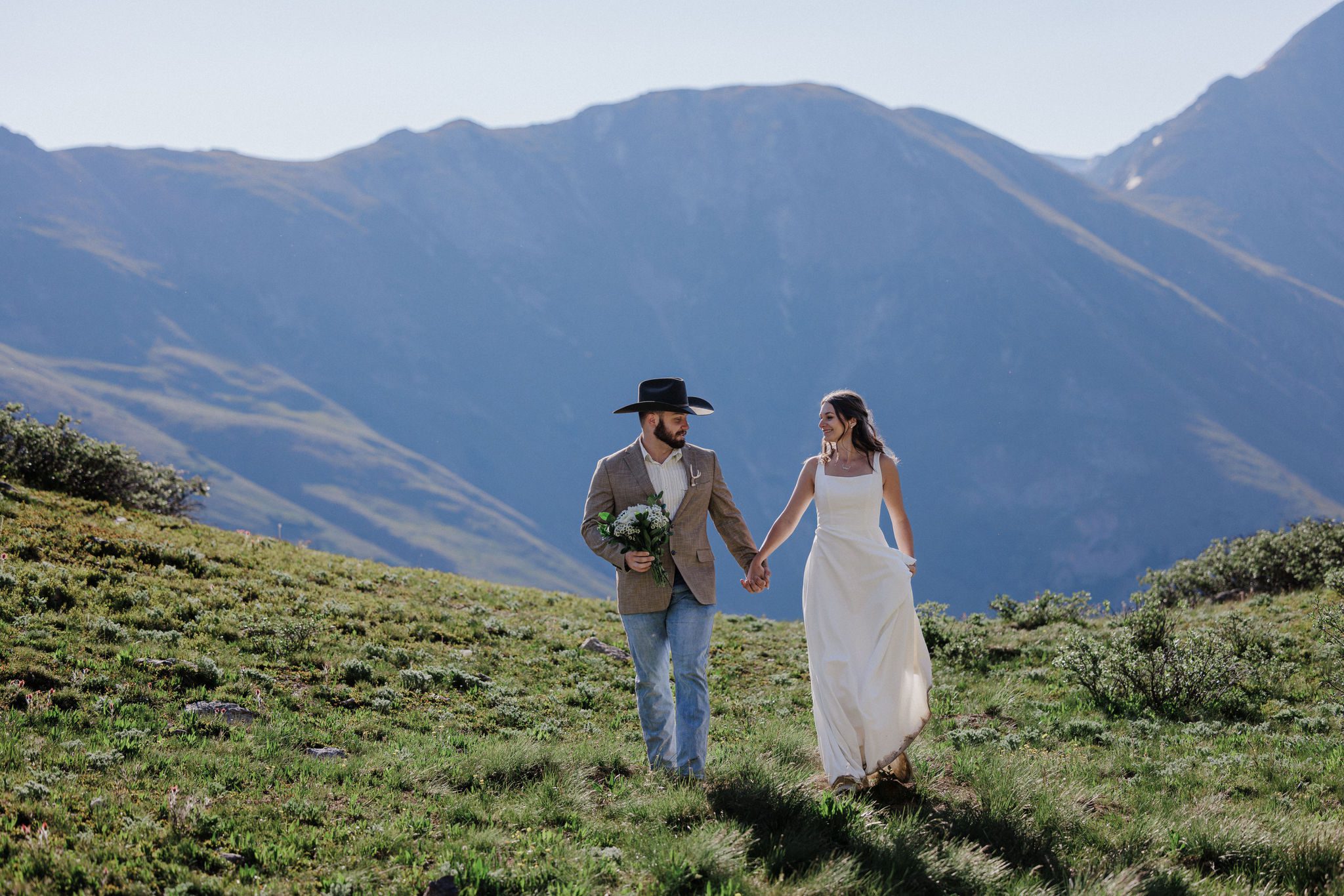 bride and groom hold hands and run through the grass in the colorado mountains during their elopement
