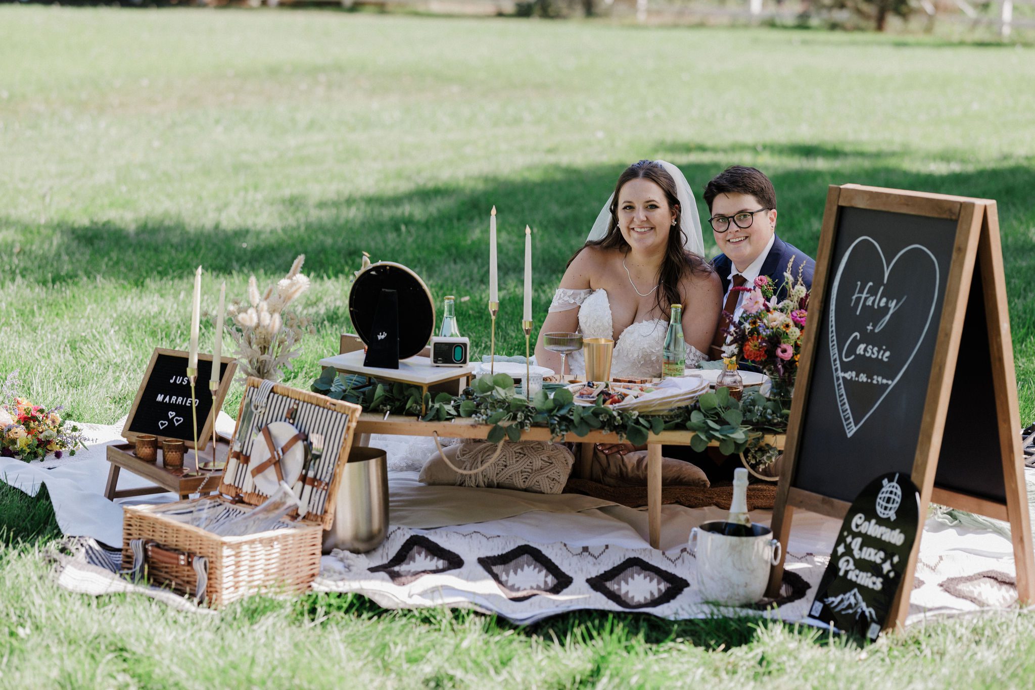 two brides smile as they sit behind luxury elopement picnic 