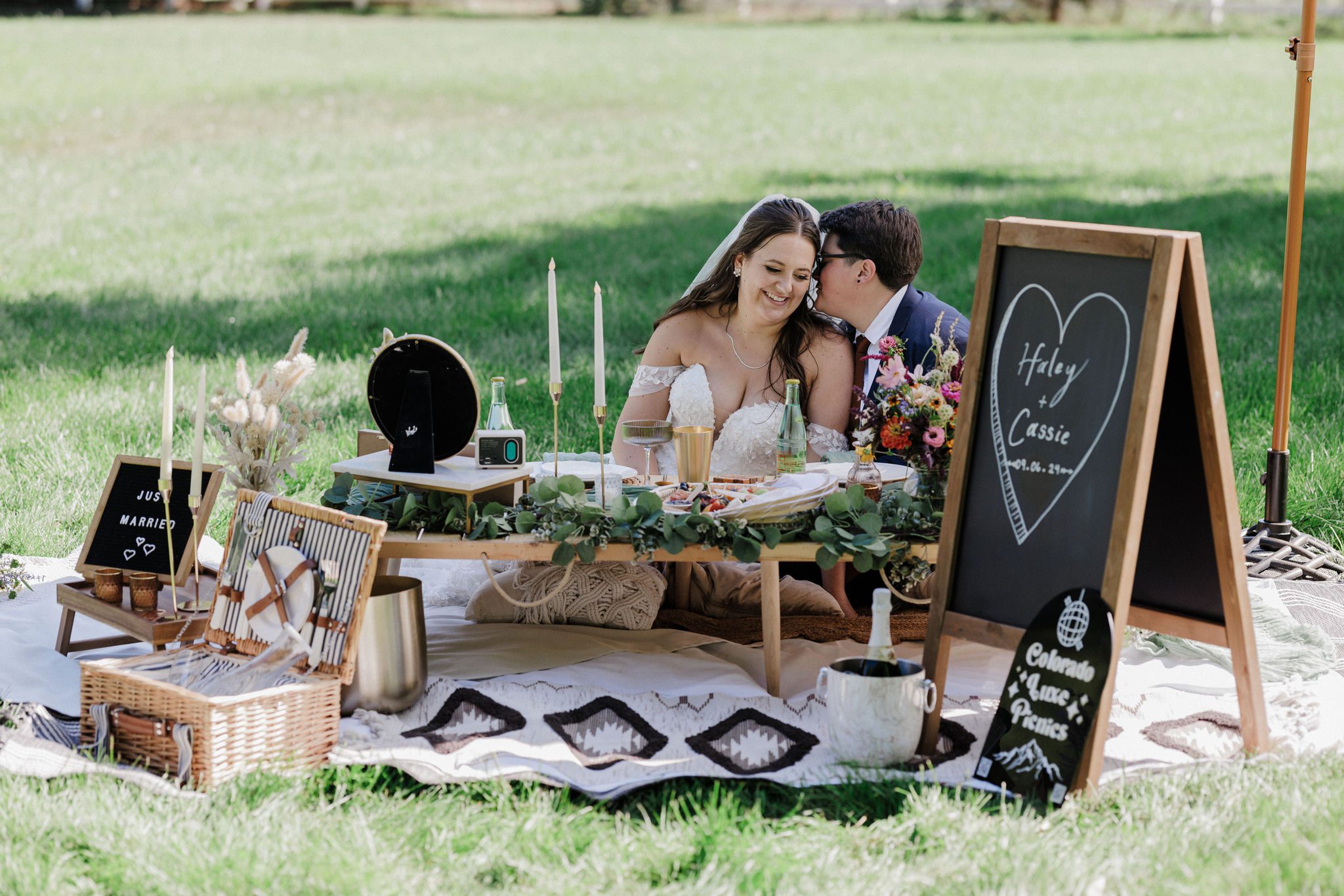 two brides sit at picnic during wedding in the backyard of an airbnb