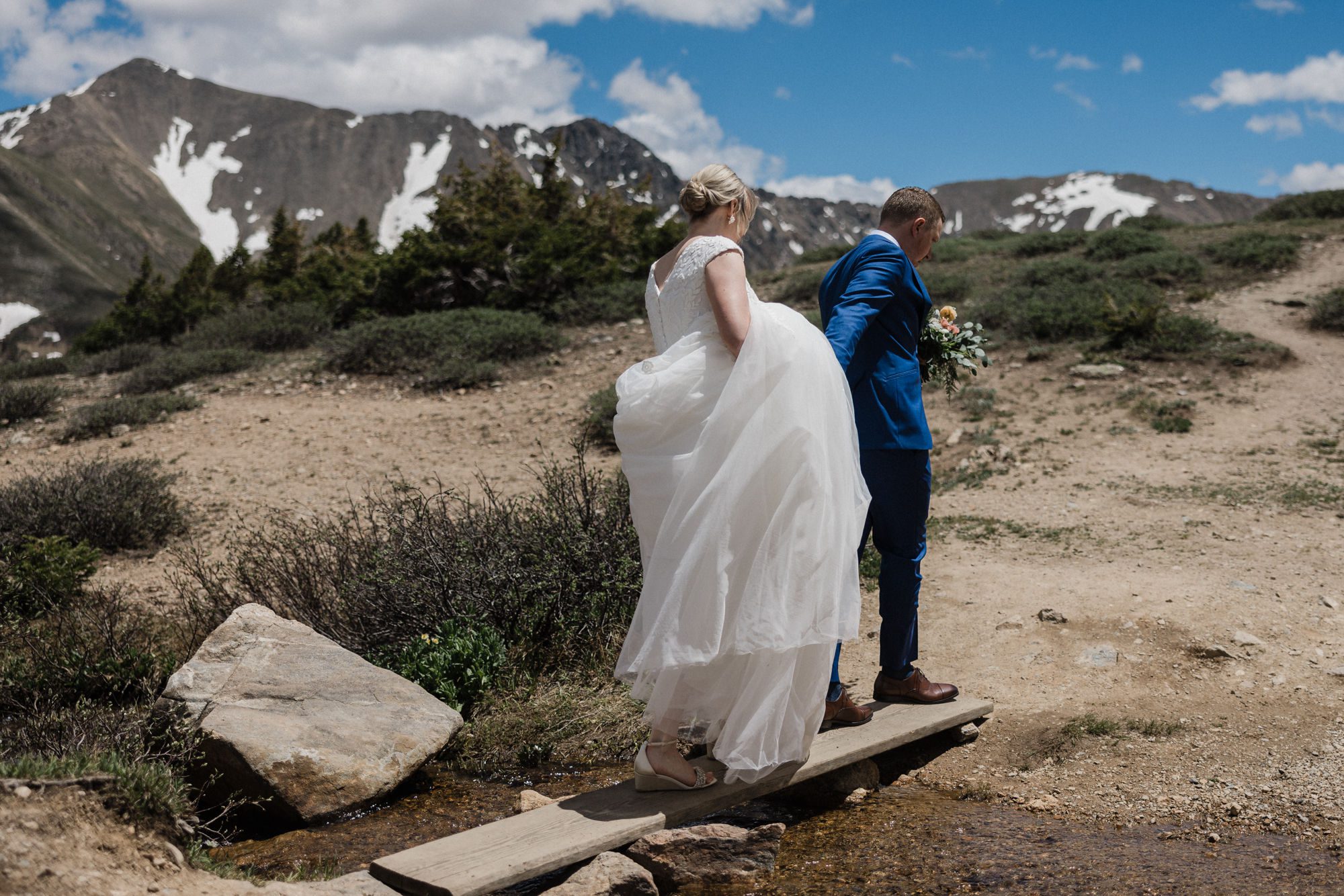 bride and groom walk across creek during mountain elopement in colorado