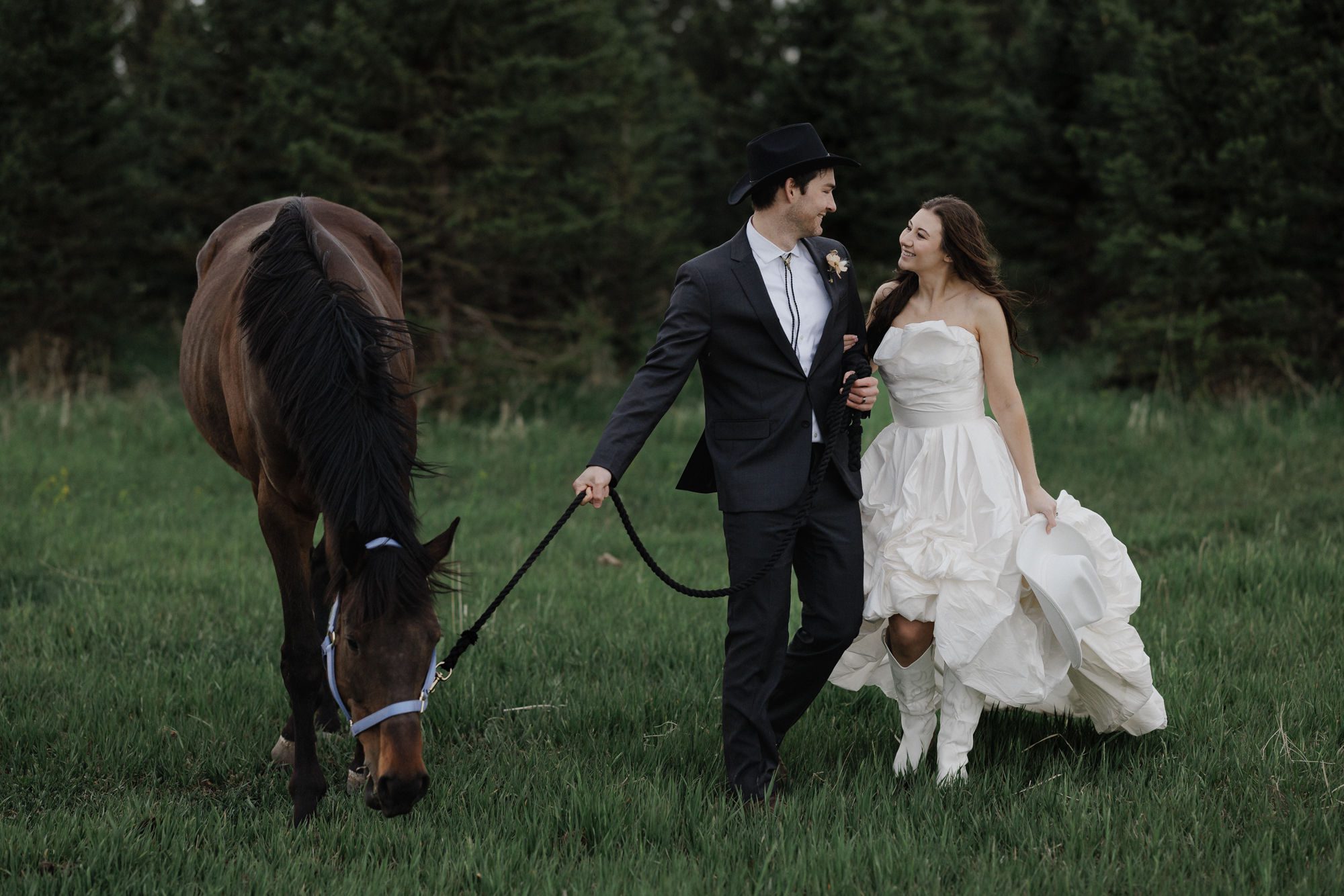 Bride and groom smile at each other and walk a horse during their colorado elopement