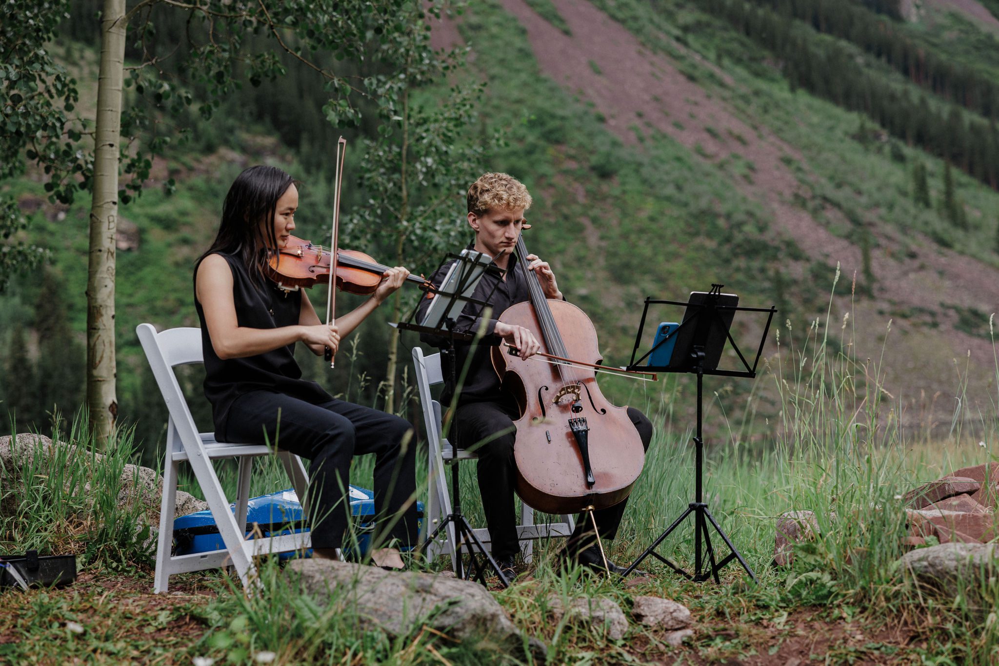 two people play live string music during a backyard wedding