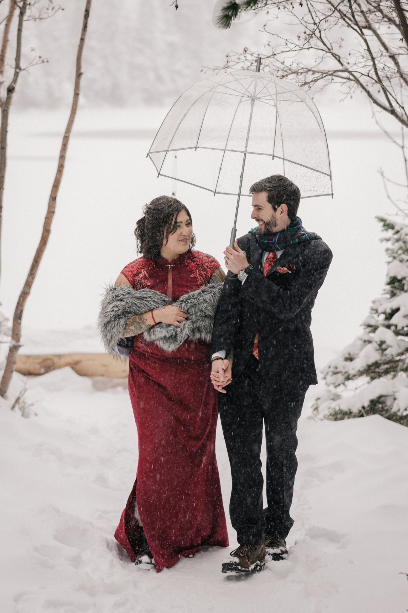 bride and groom hold clear umbrella and walk along trail at RMNP during their winter elopement