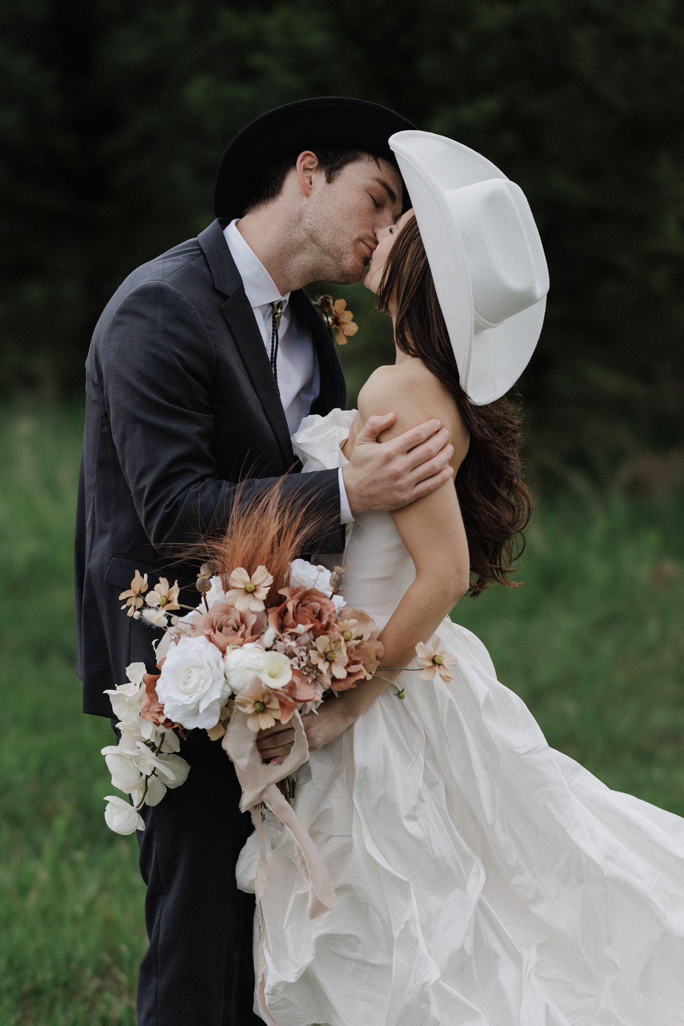 bride and groom in western hats kiss during wedding photos in colorado