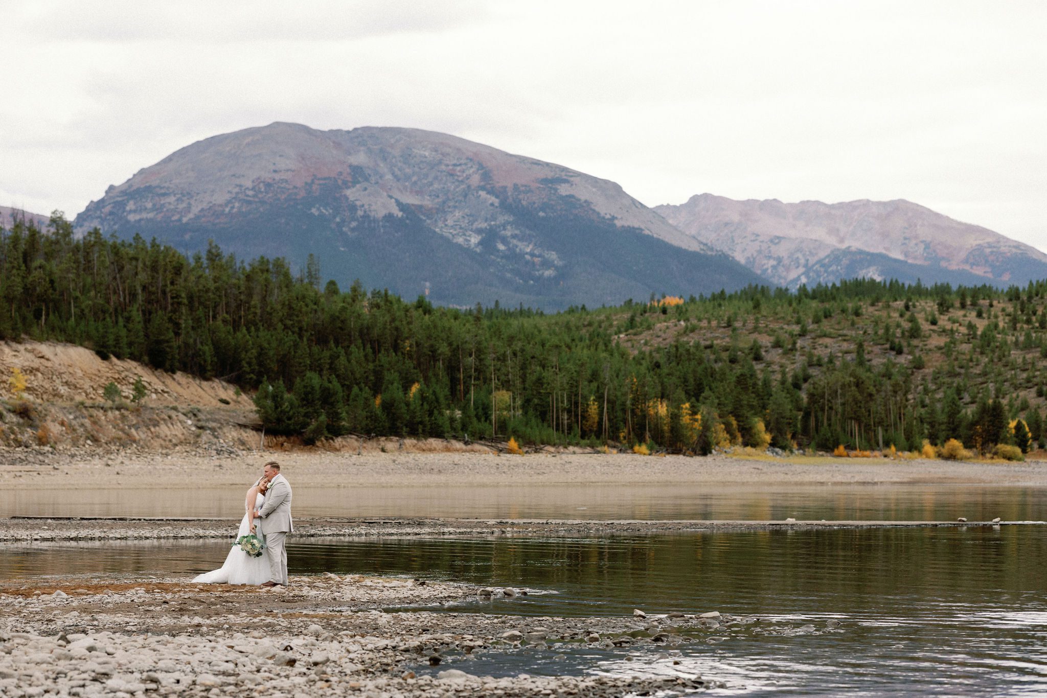 bride and groom stand at the edge of the lake during wedding photos 