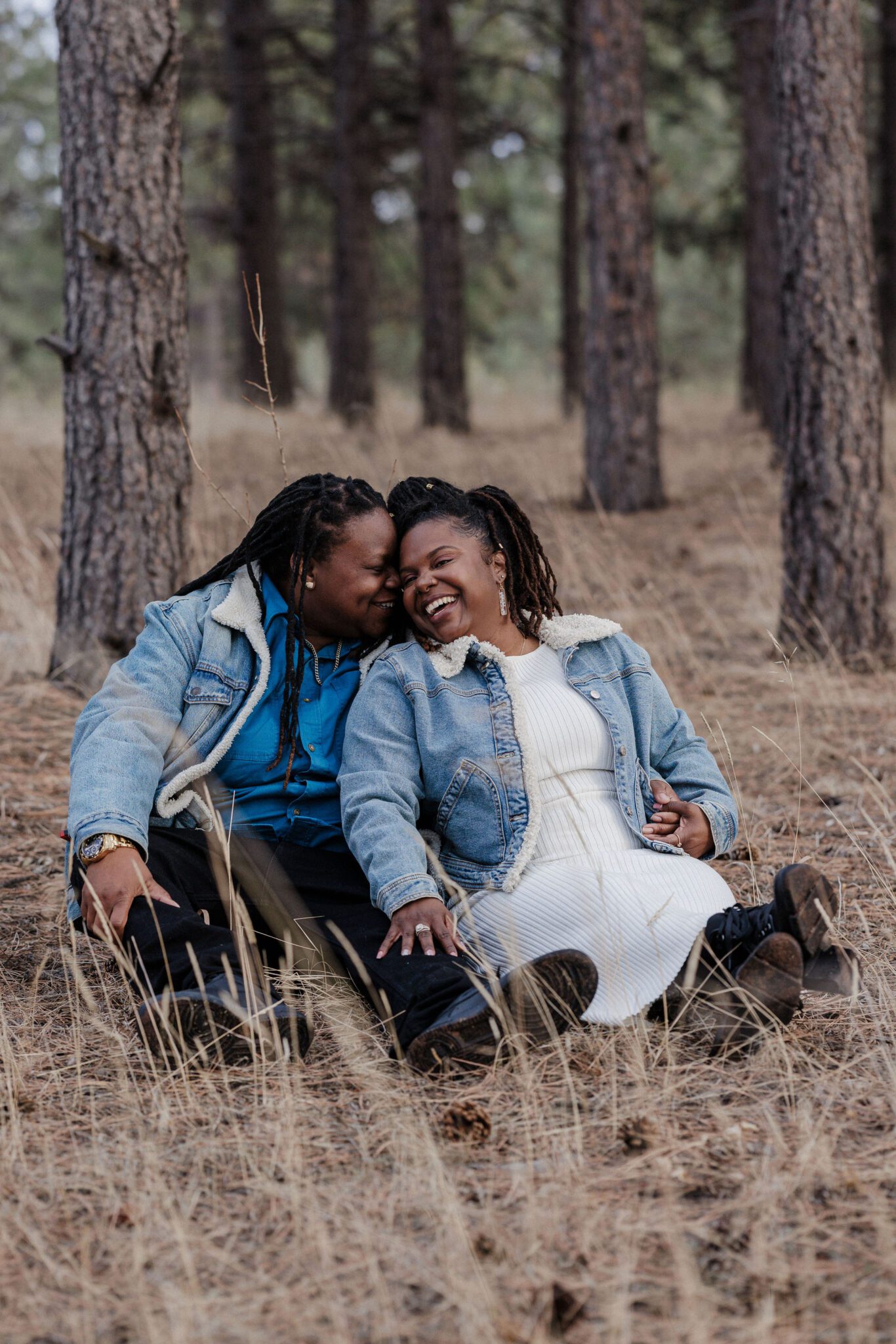lgbtq+ couple sits on ground and poses for colorado engagement photos at manitou lake