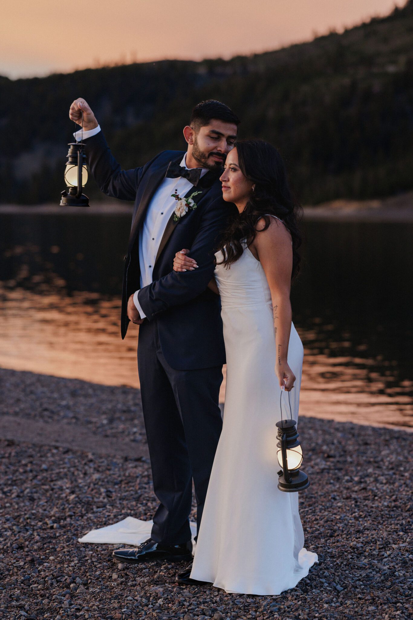 bride and groom stand arm in arm, groom reaches over to kiss brides head during sunset photos at popular colorado elopement venue, lake dillon