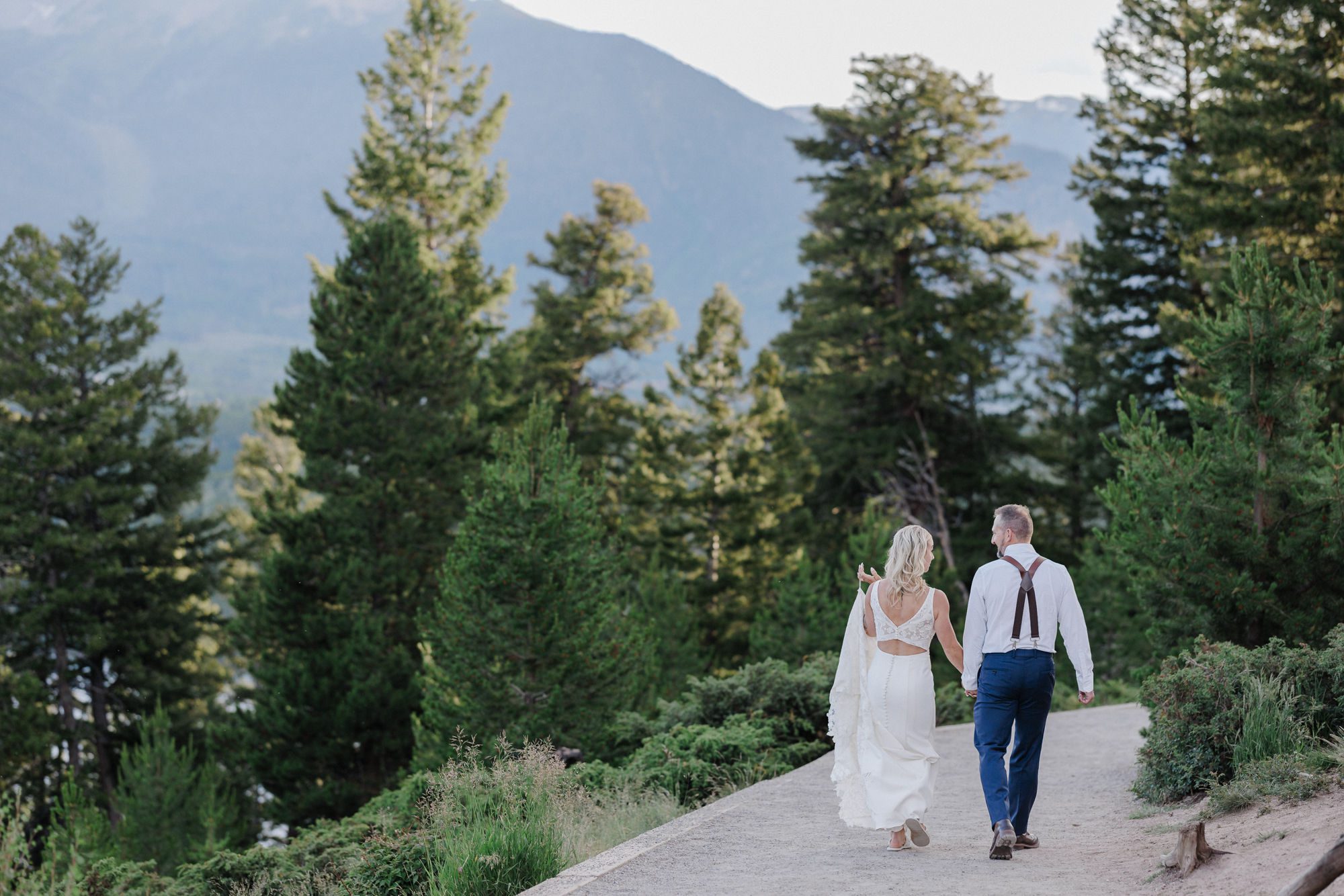 bride and groom hold hands and walk through the trees during wedding photos