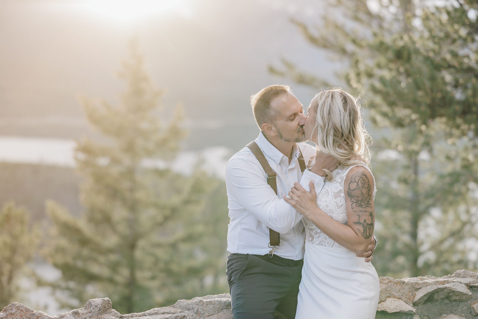 bride and groom sit on ledge and kiss during sunset wedding photos