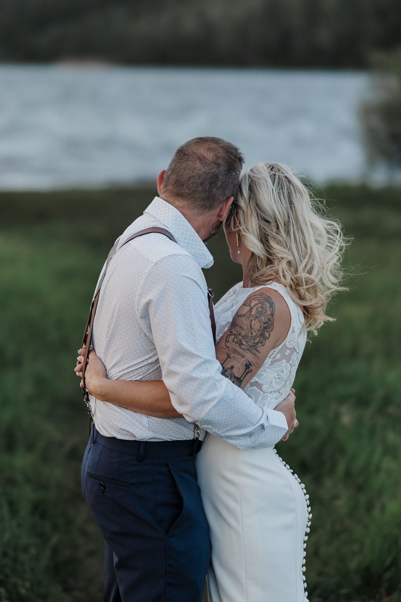 bride and groom hug beside the edge of the lake during wedding photos