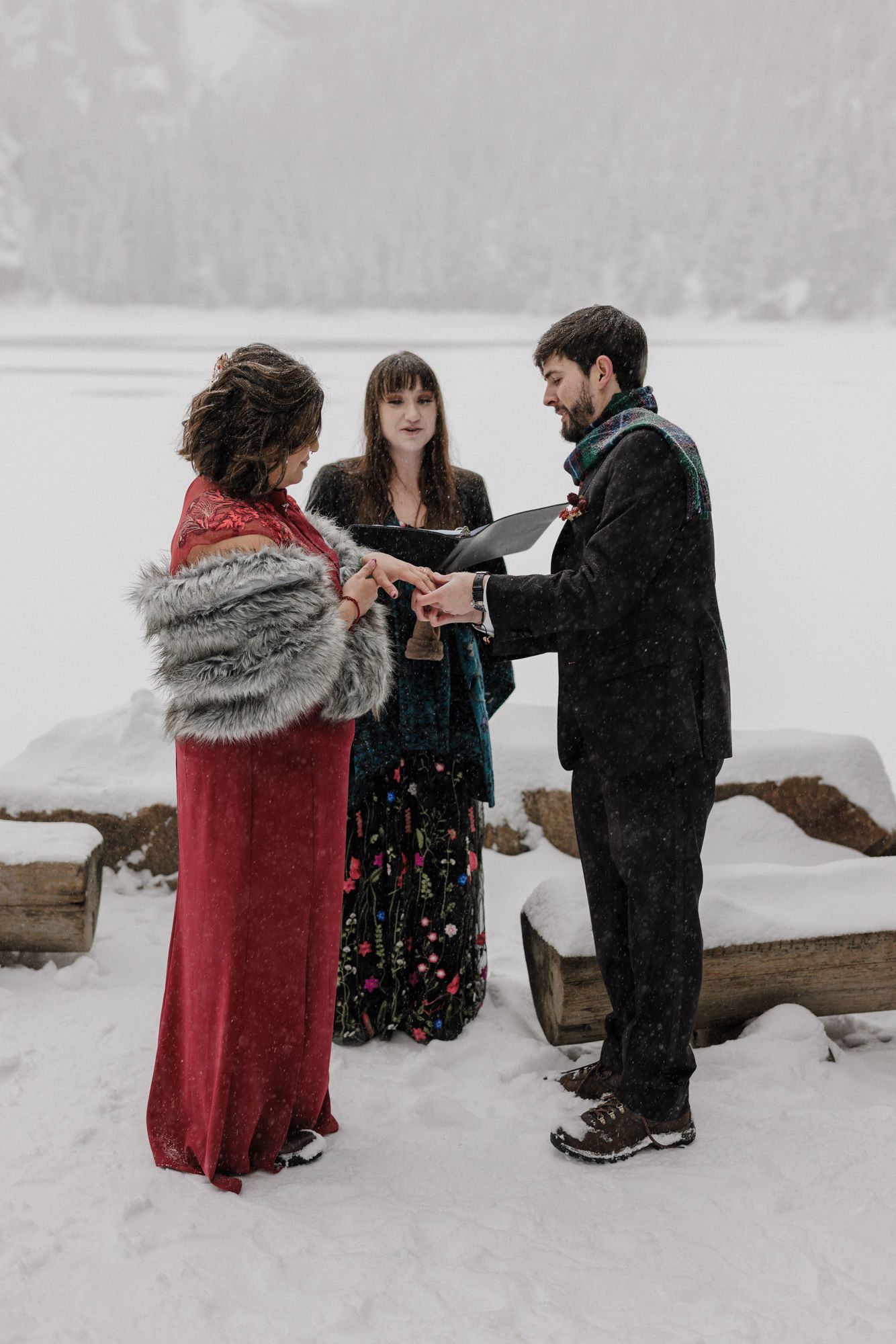 bride and groom put wedding rings on each other at rocky mountain national park during snowfall