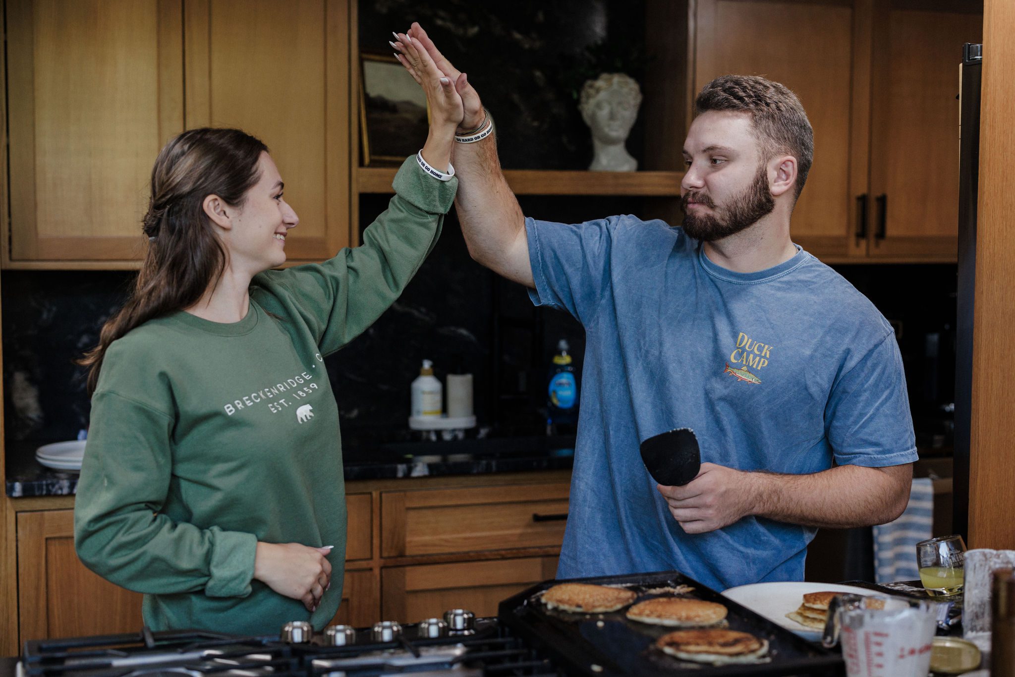 engaged couple high fives while making pancakes after proposing in colorado