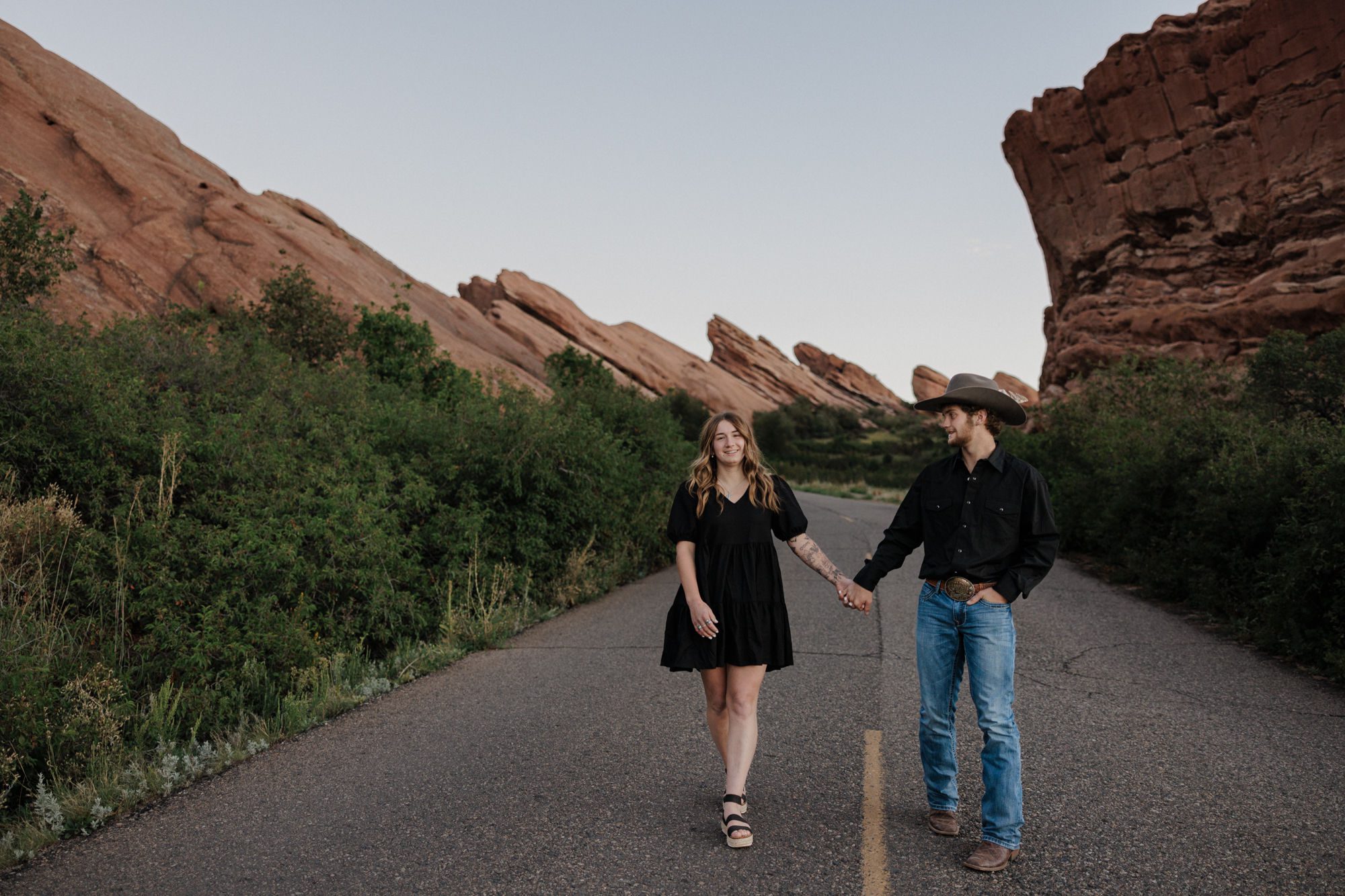 man and woman hold hands and walk across road at colorado proposal location