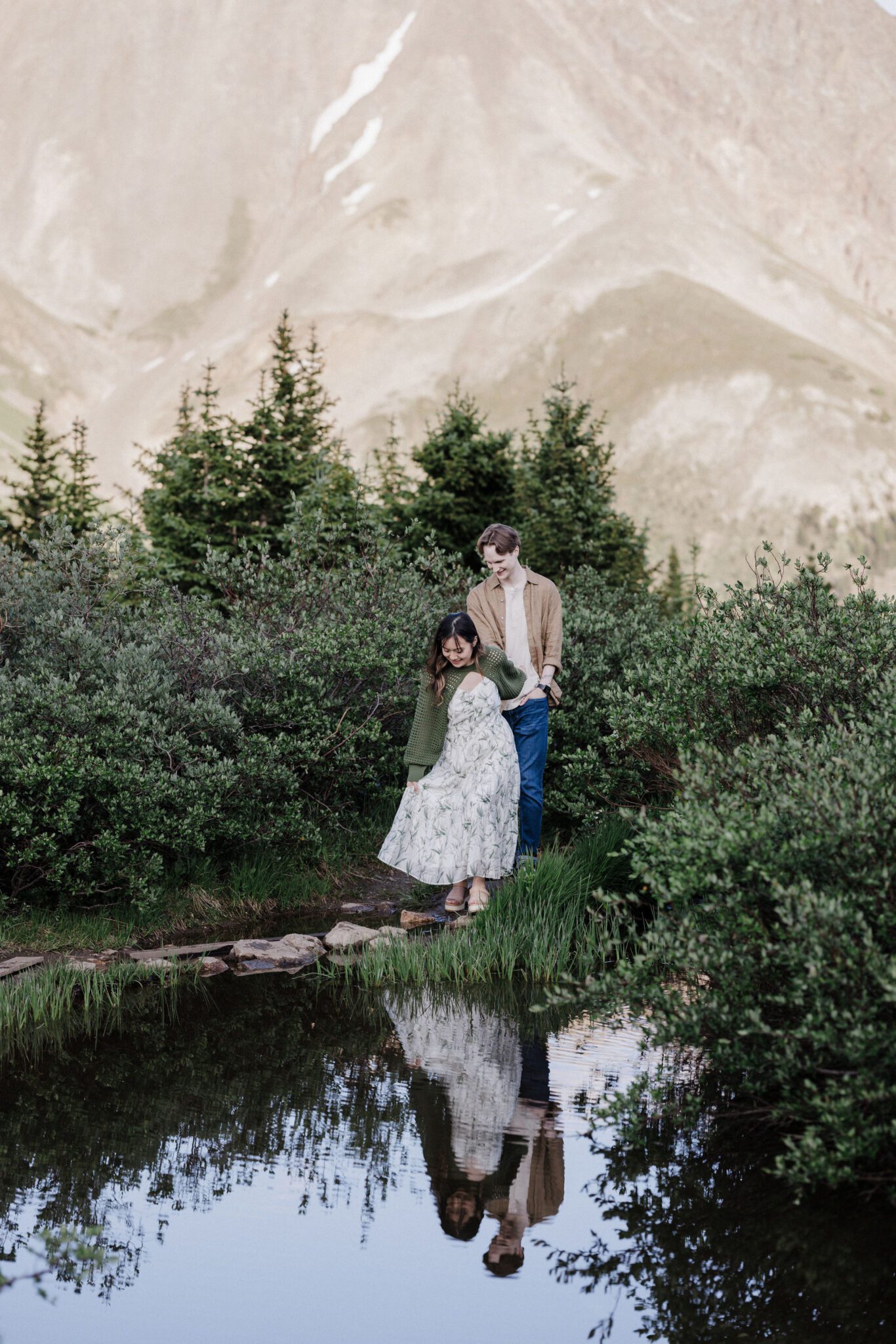 after choosing the best place to propose in colorado, engaged couple holds hands and walks along alpine lake
