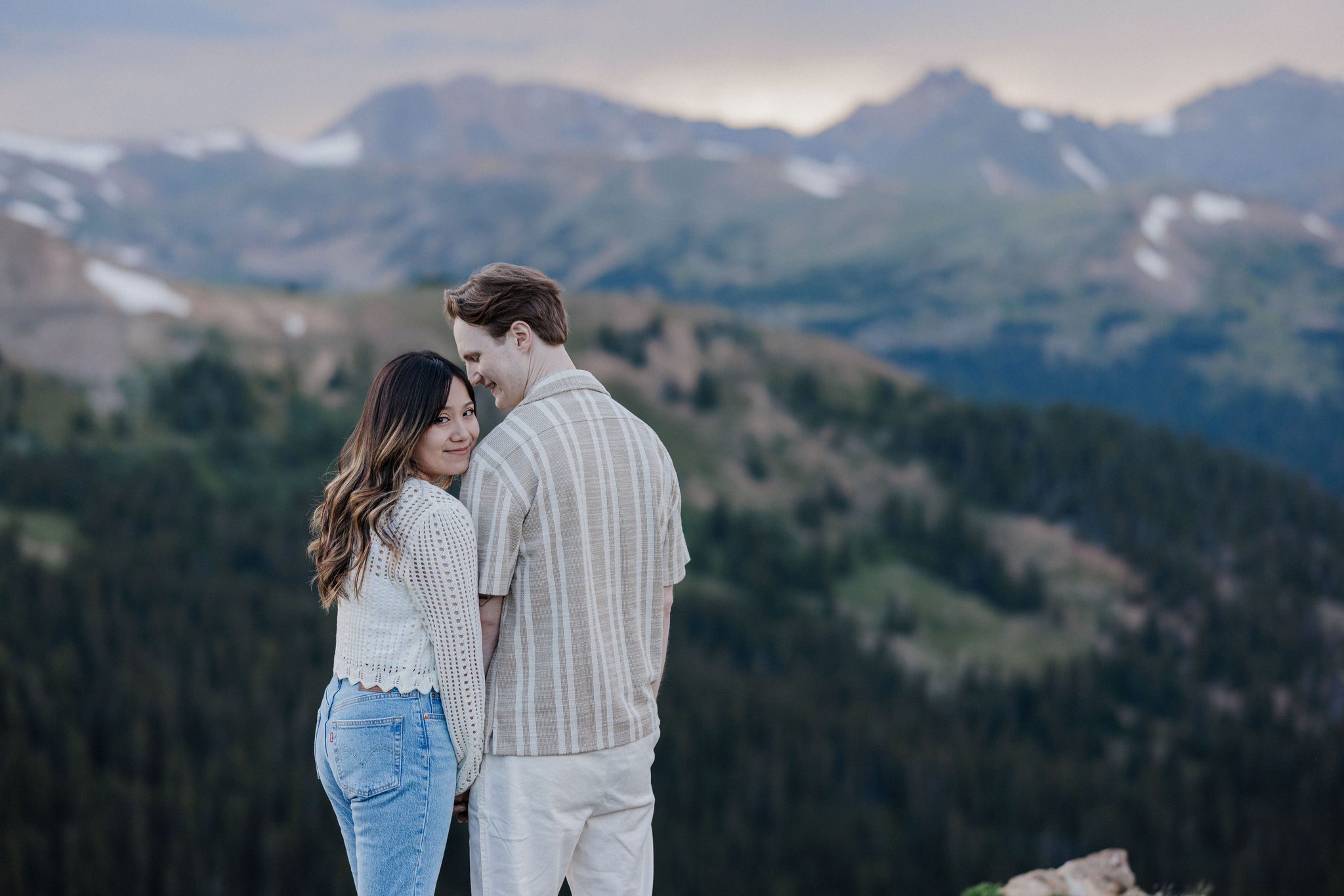 woman leans head on mans shoulder and looks at photosgrapher while taking proposal photos in colorado