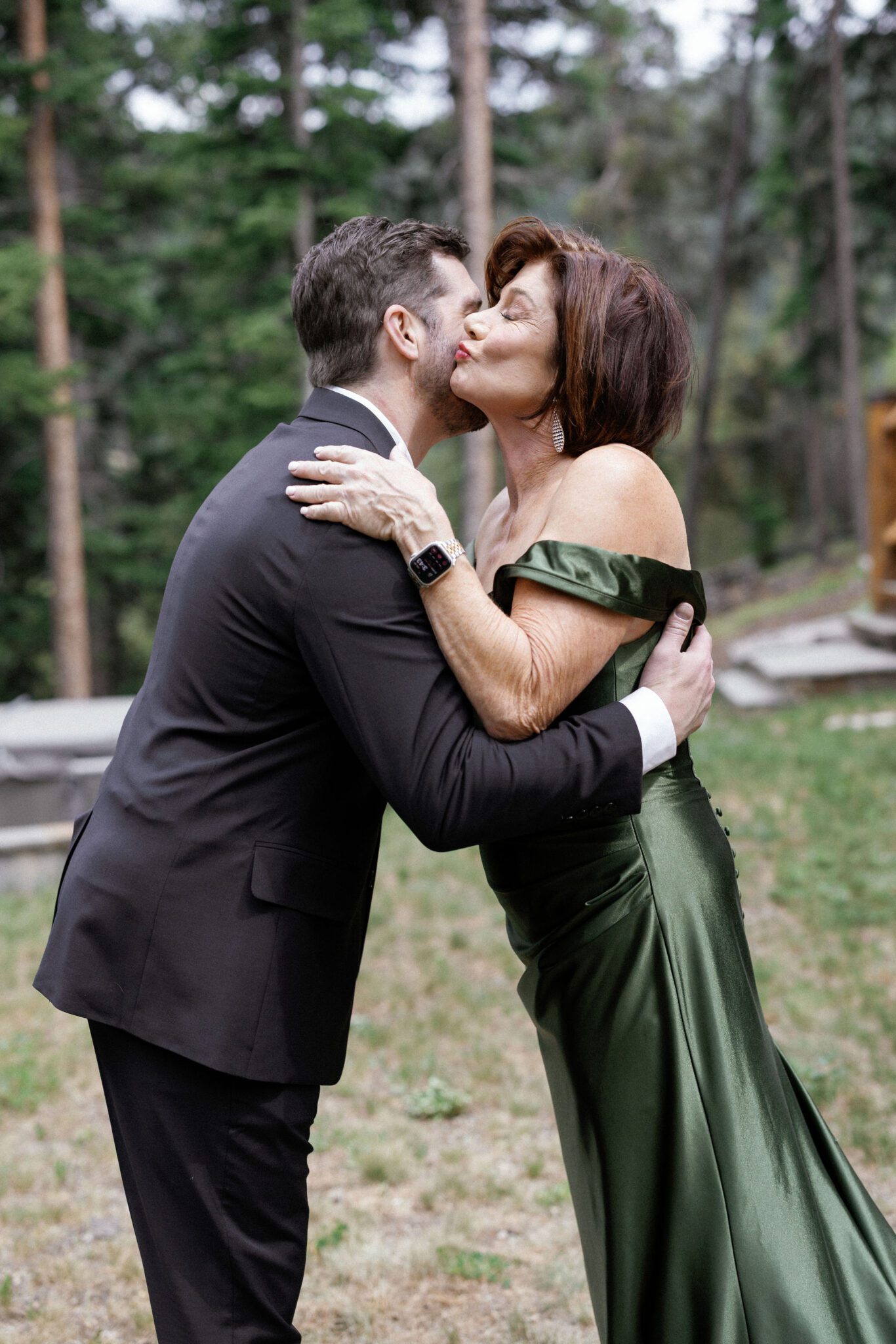 mother of the bride leans over and kisses her son's cheek