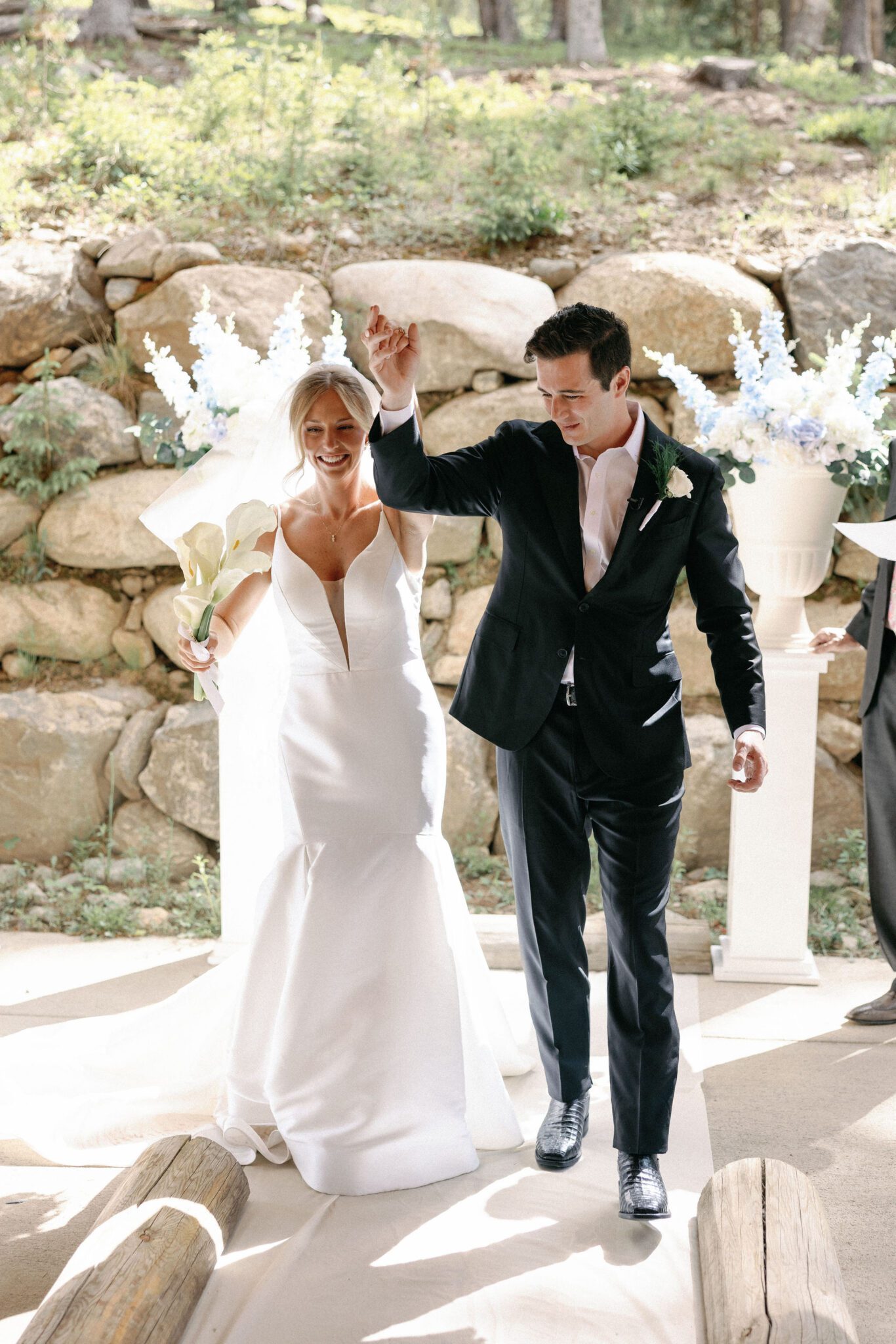 bride and groom smile and raise their hands as they walk back down the aisle