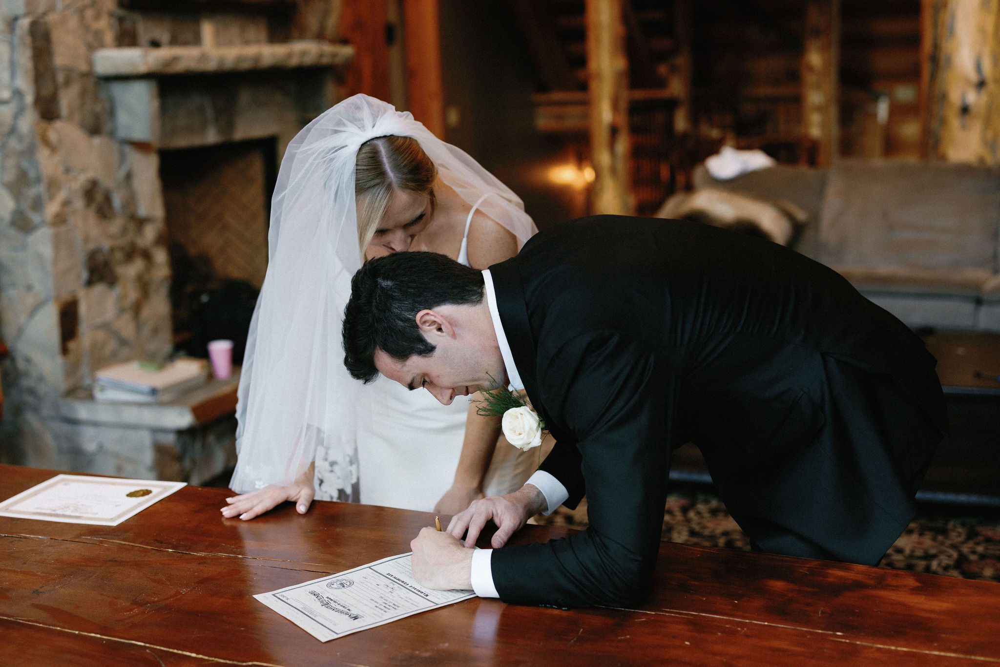 bride and groom lean over table and sign their colorado marriage license