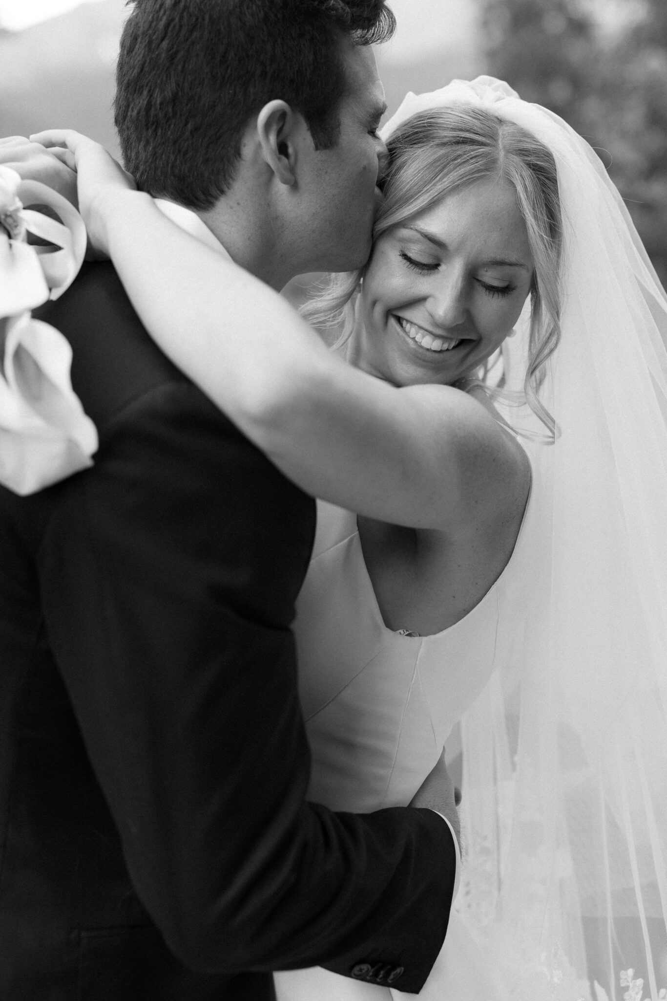 groom kisses brides head and she smiles during wedding photos