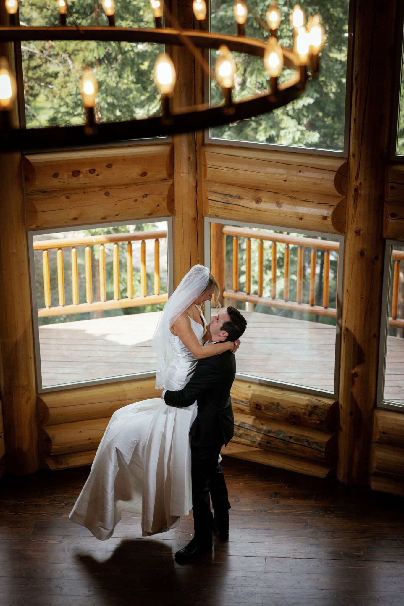 groom lifts up bride in front of the large windows in the airbnb during wedding photos
