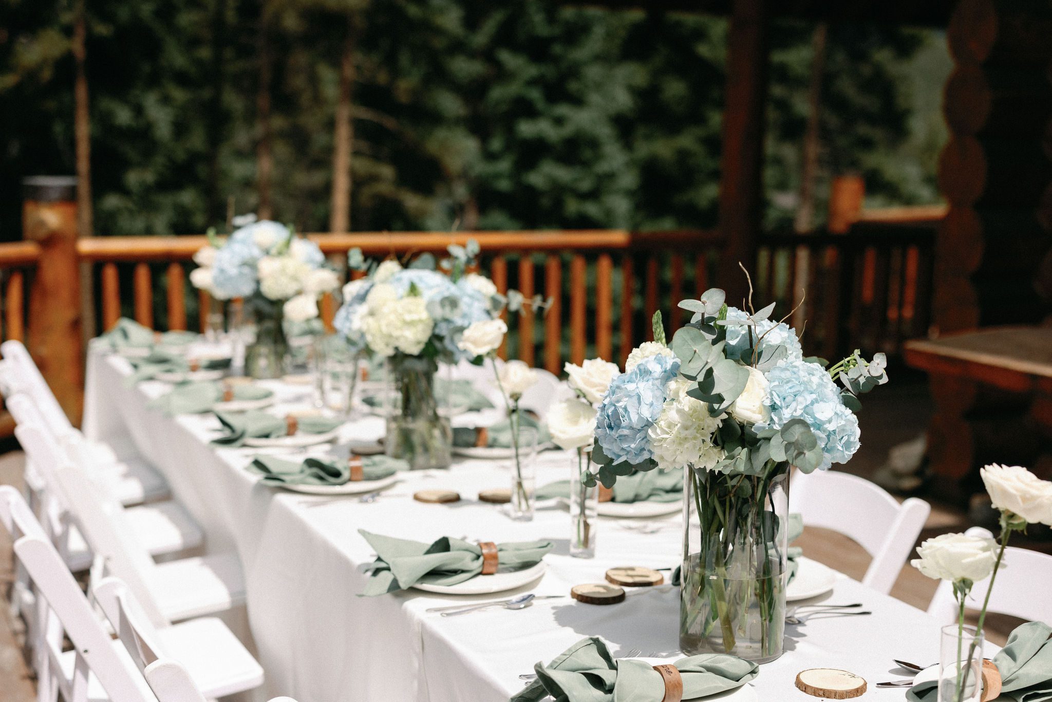 a table on the deck of an airbnb is set up for a wedding reception dinner outside