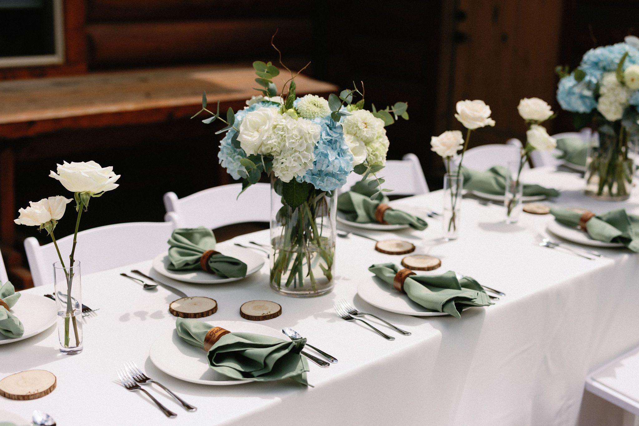 a table on the deck of an airbnb is set up with green, white, and blue details for a wedding reception