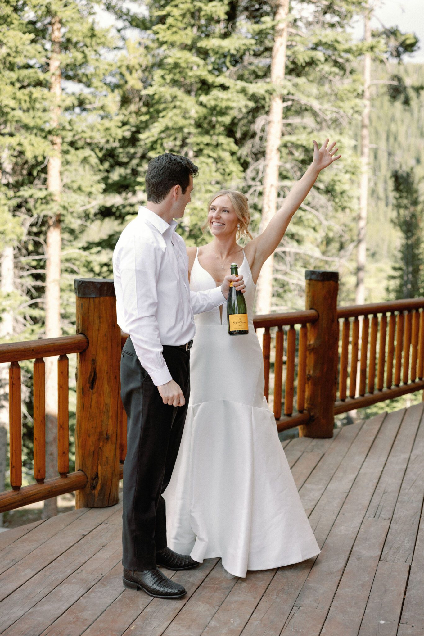 bride and groom smile as they pop a bottle of champagne