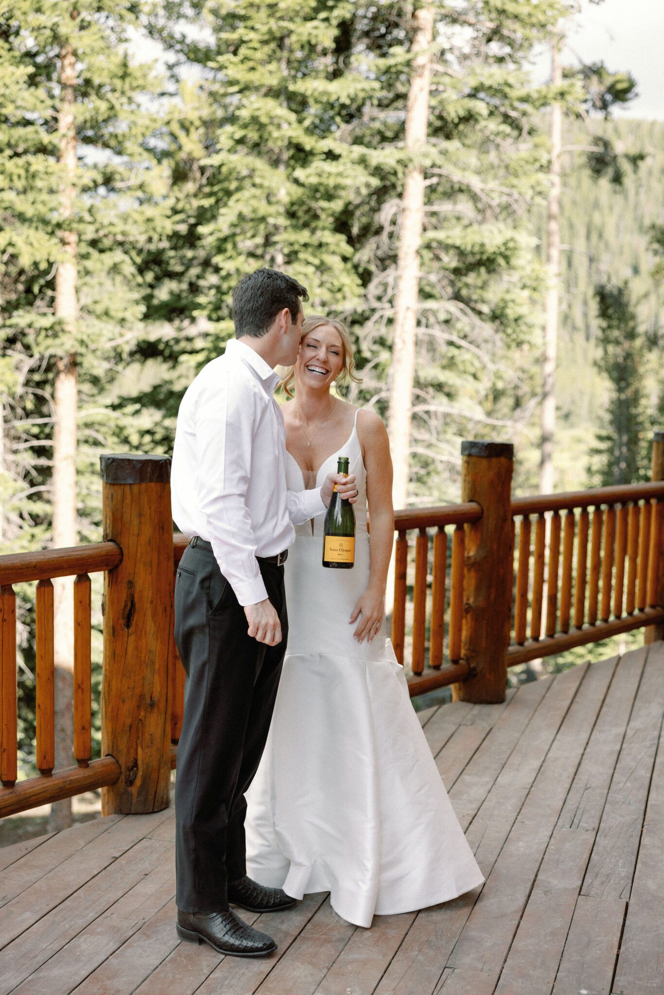 groom kisses brides cheek before they pop a bottle of champagne