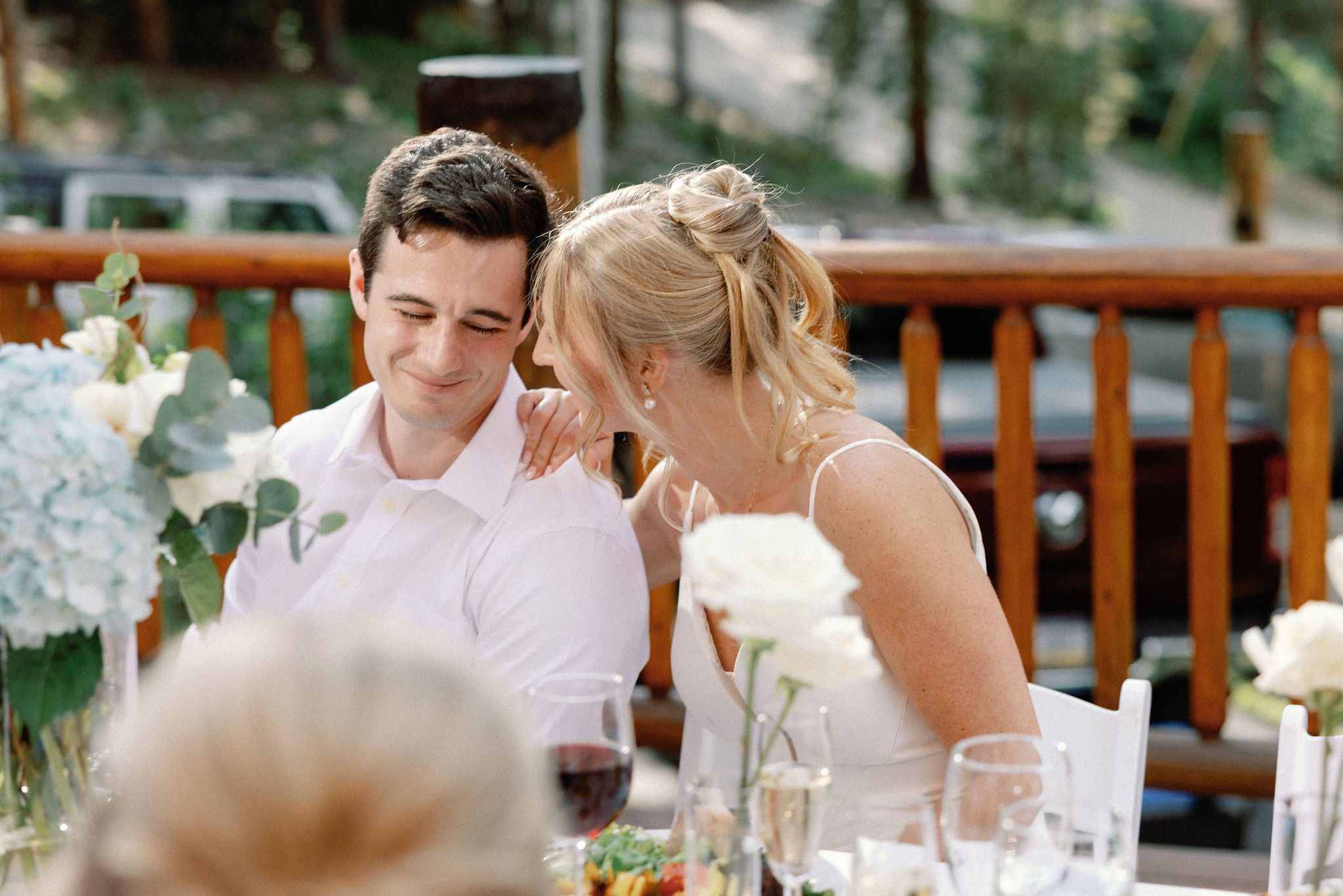 bride and groom lean on each other and smile as they listen to wedding toasts during the reception dinner