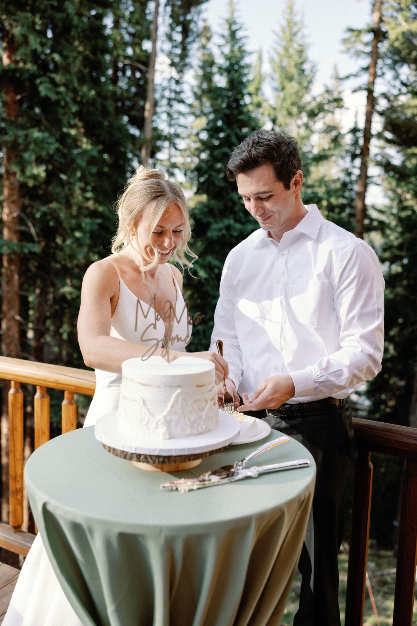 bride and groom smile as they place a piece of wedding cake on a plate after they cut it
