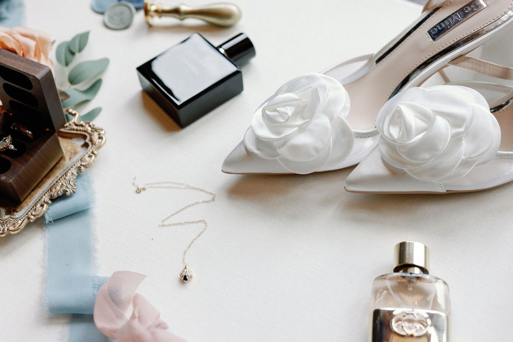 wedding flat lay photo with white wedding heels, ring box, necklace, and perfumes