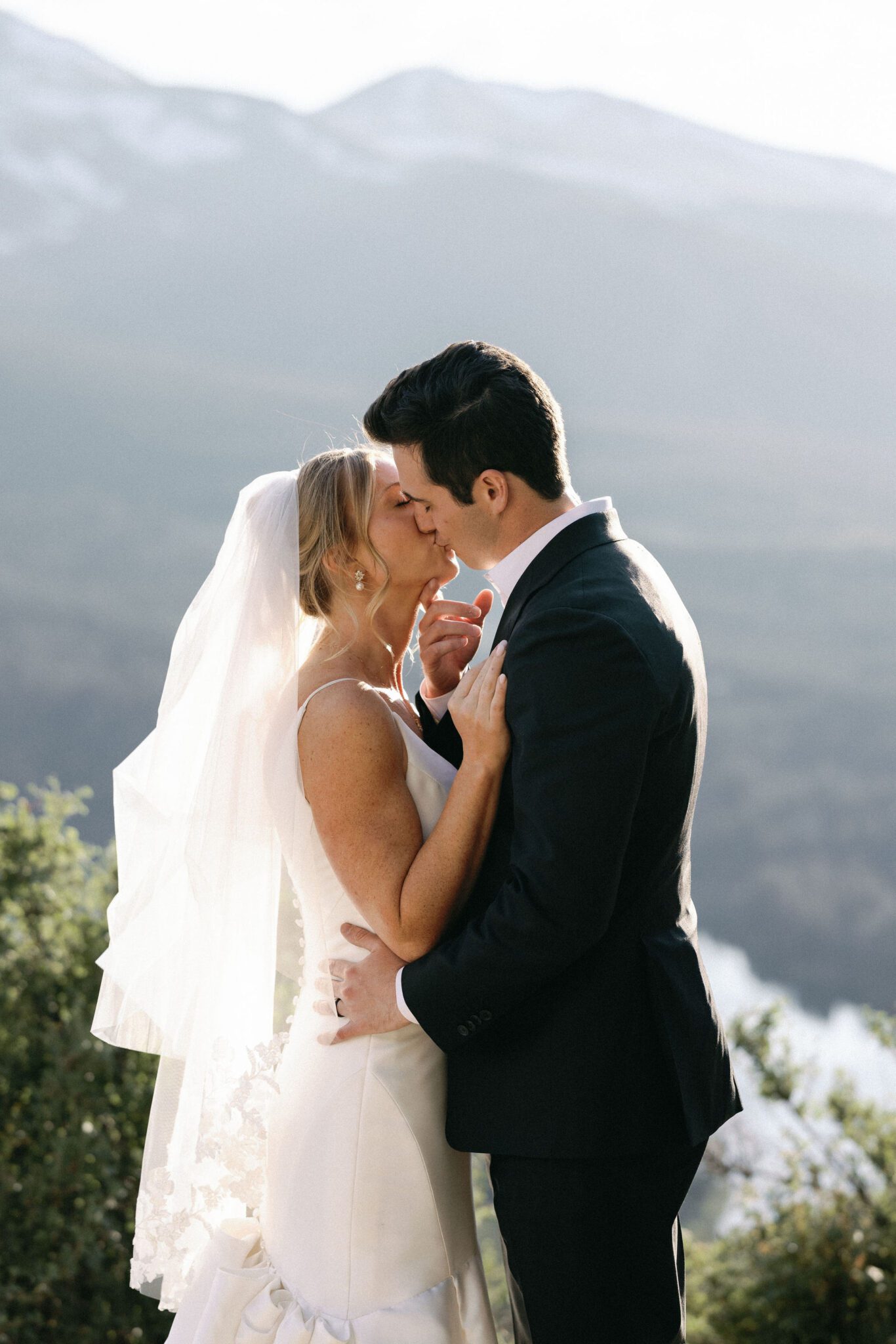 bride and groom kiss with mountains in the background