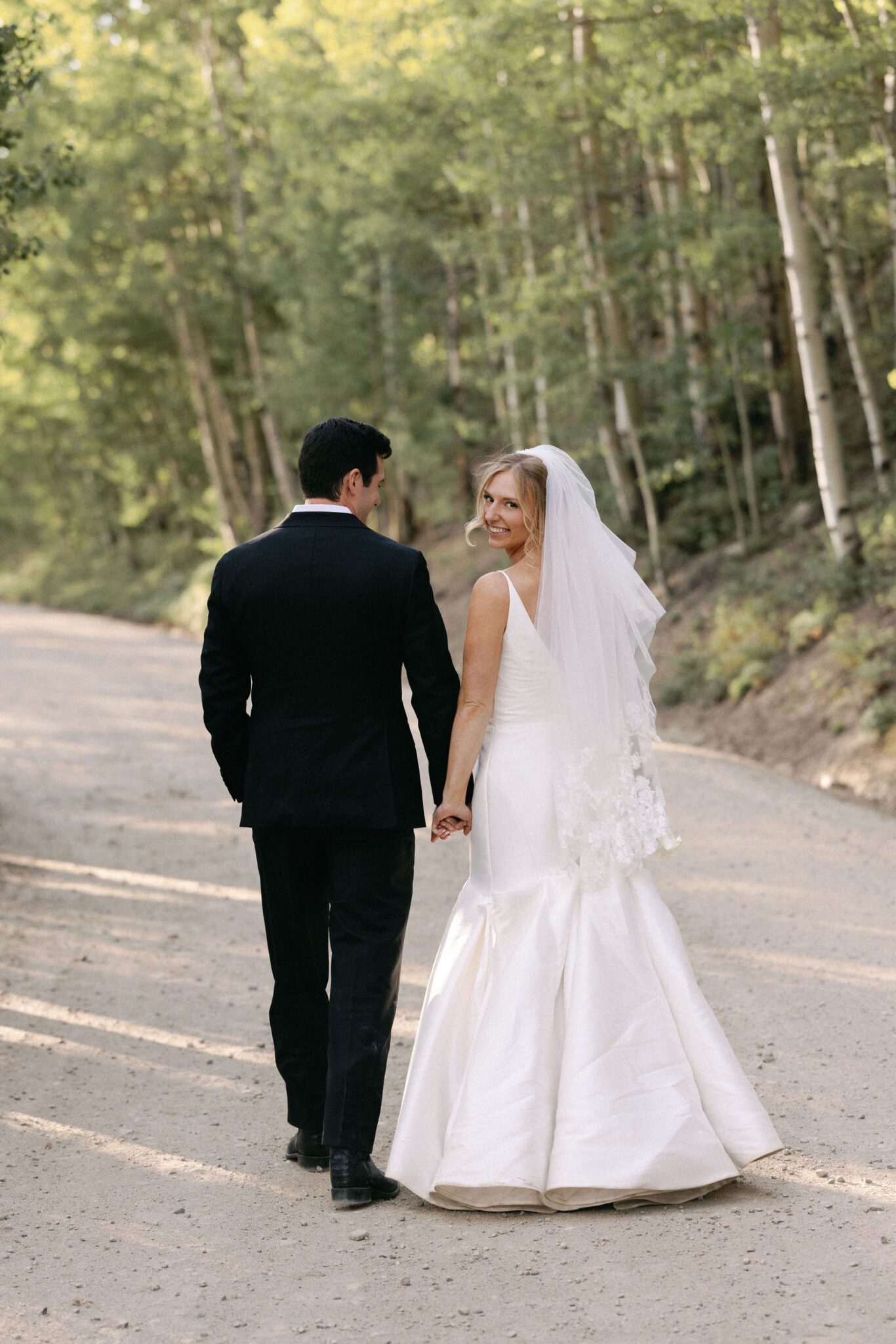 bride and groom hold hands and walk down the dirt road during wedding photos