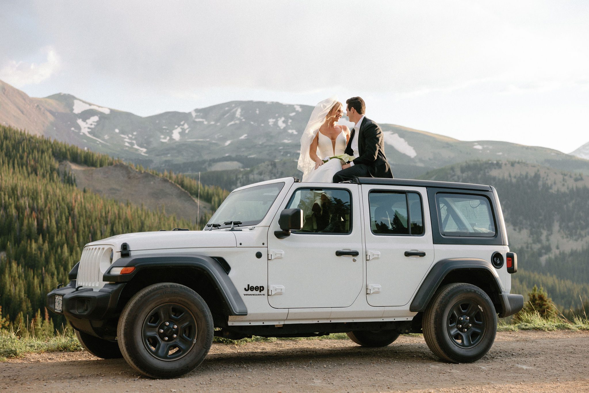 bride and groom sit on the top of their white jeep during wedding photos at boreas pass