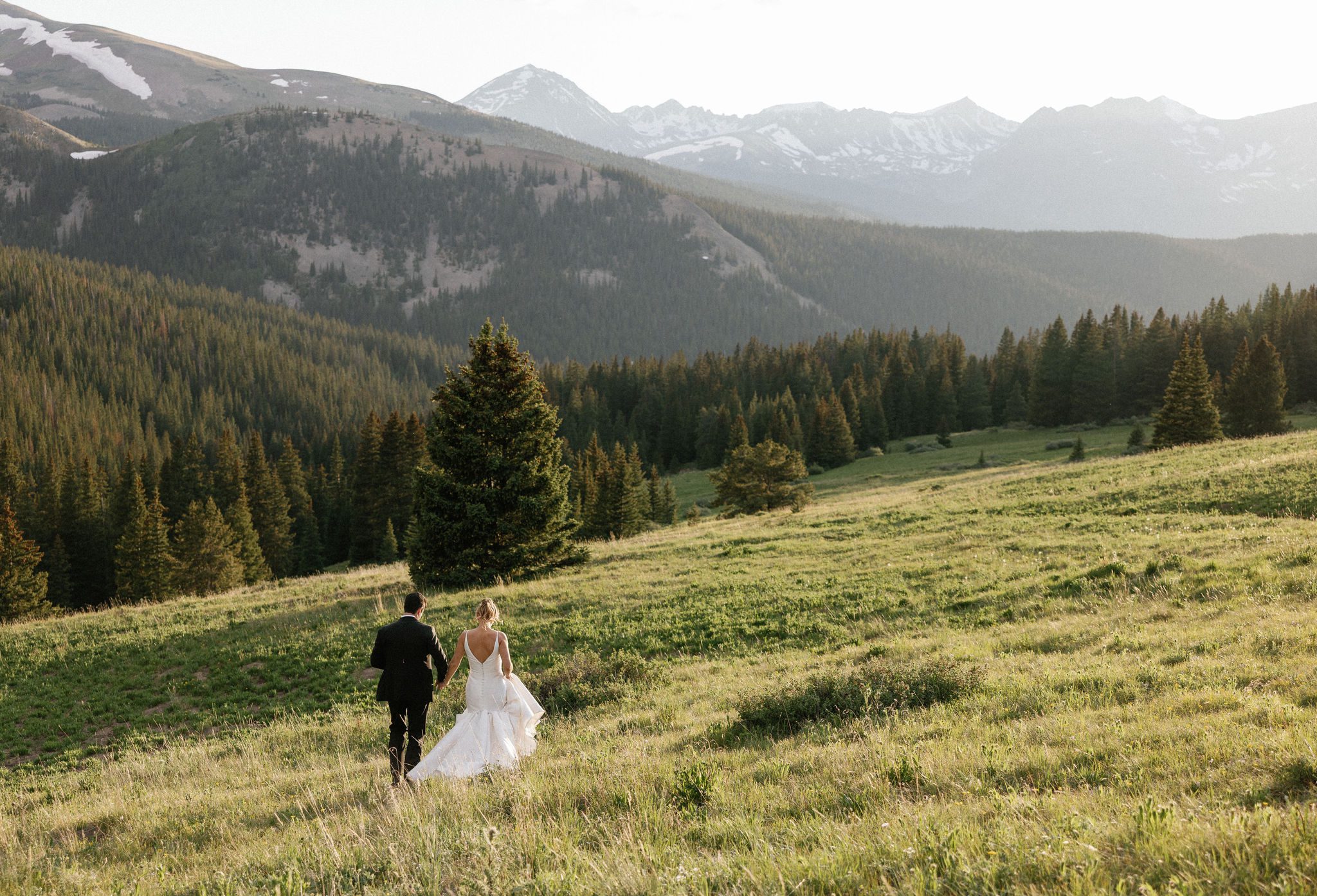 after colorado airbnb wedding, bride and groom hold hands and walk into the mountains during sunset