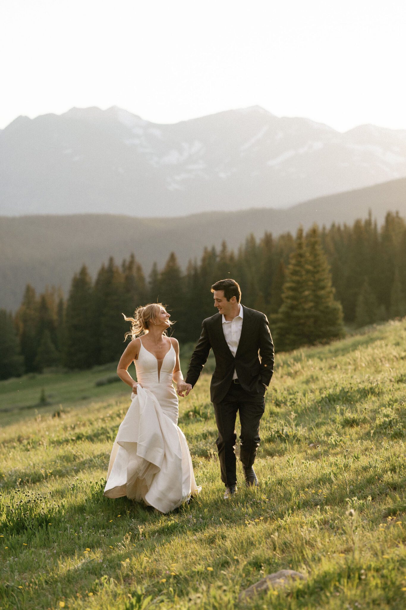 bride and groom hold hands, smile and laugh, and run on a grassy slope in the mountains during sunset at boreas pass