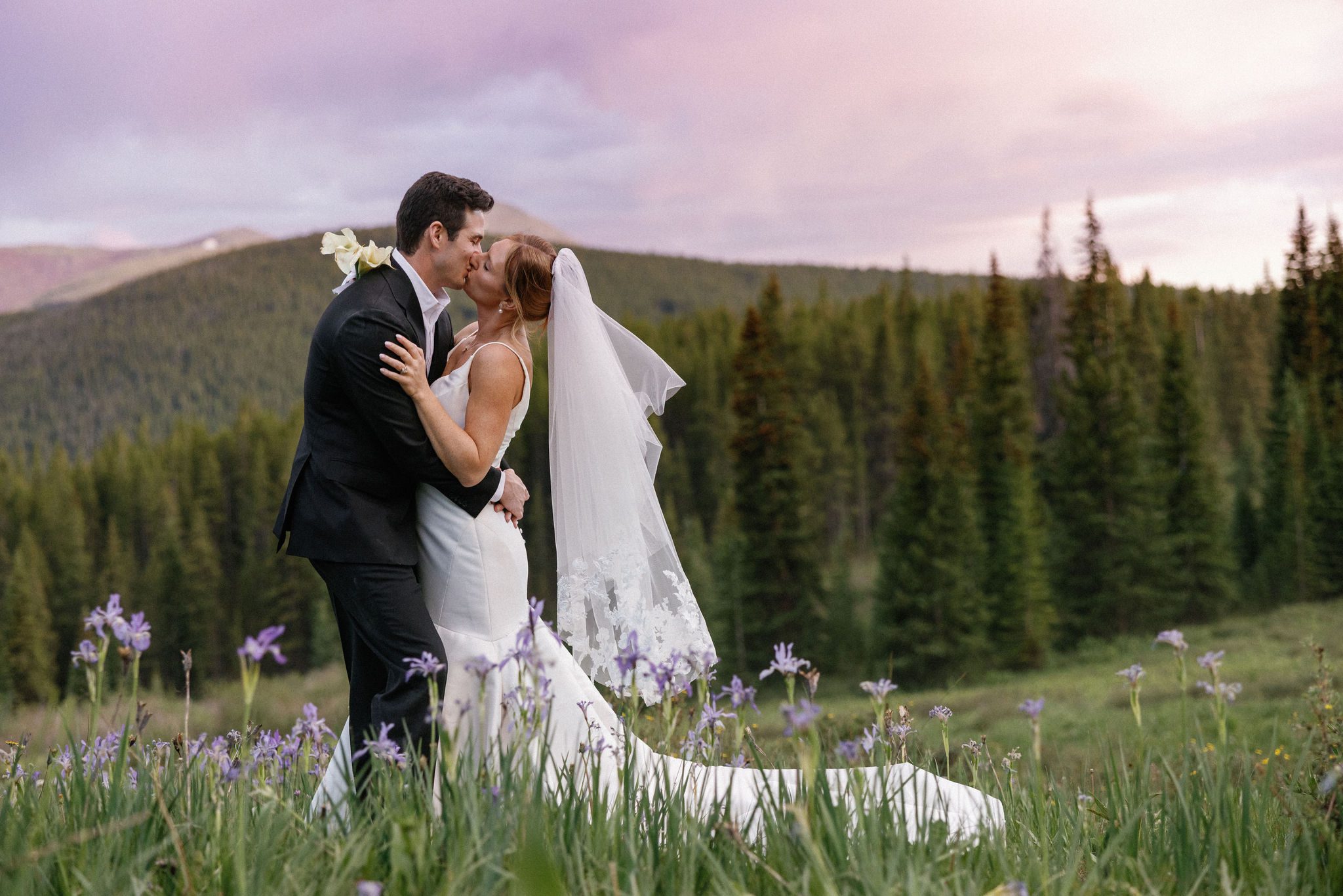 after their colorado airbnb wedding, bride and groom stand in the mountain wildflowers and share a kiss