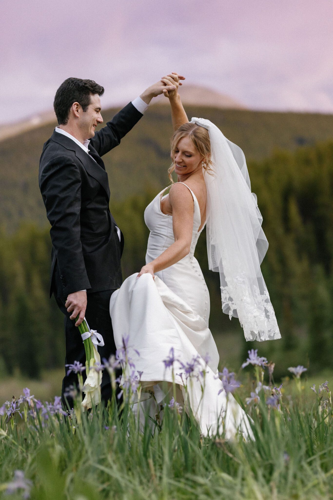 groom twirls bride in a field of purple wildflowers during sunset, after colorado airbnb wedding