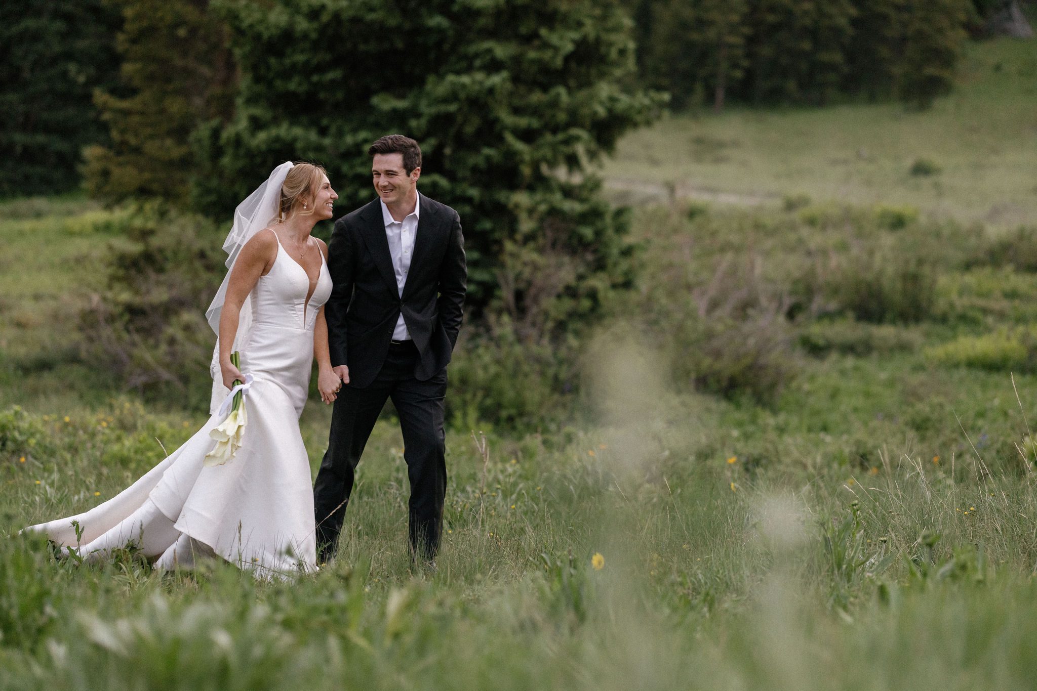 bride and groom hold hands and walk through a field in the colorado mountains