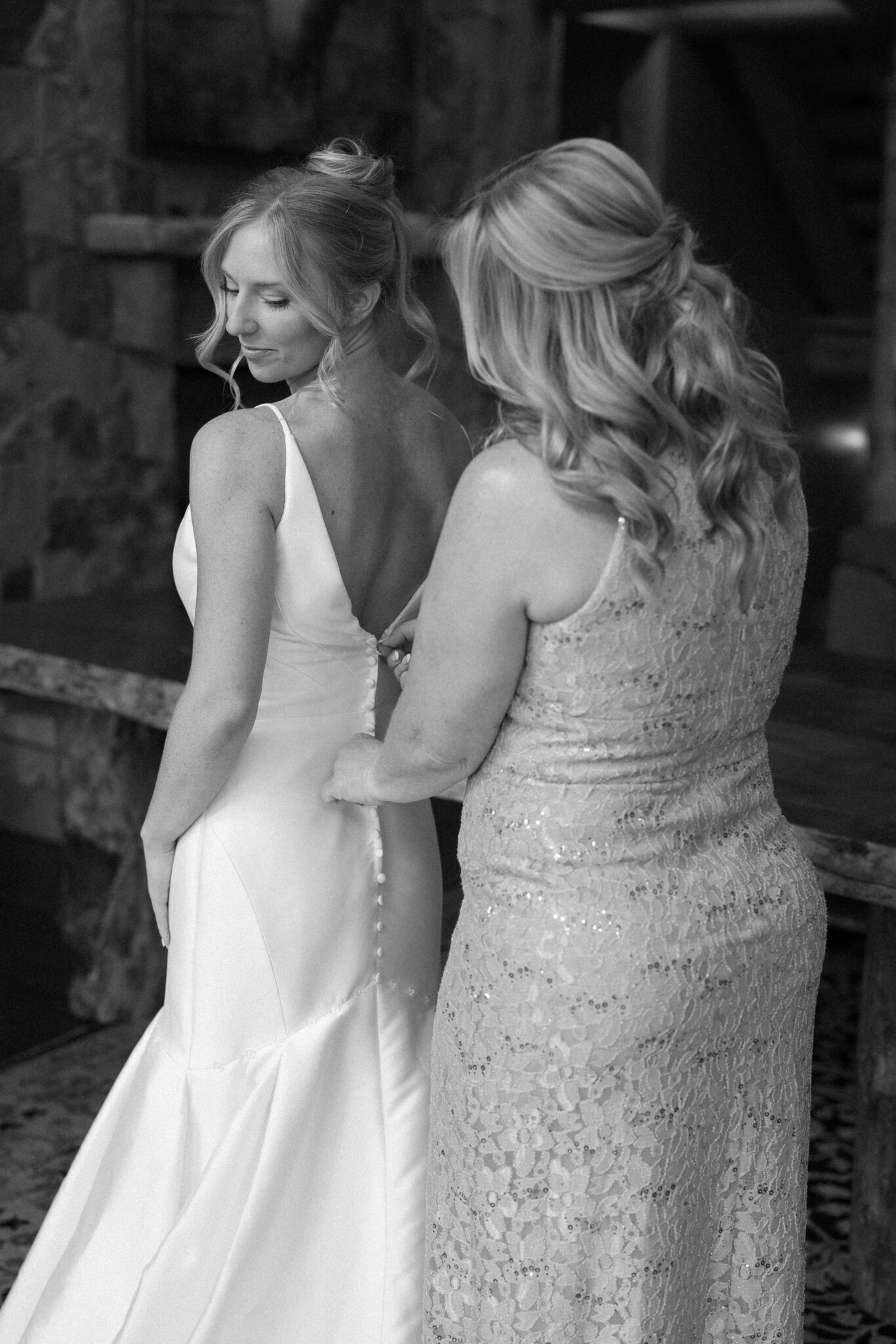 bride looks back at mother as she helps the bride by buttoning her wedding dress