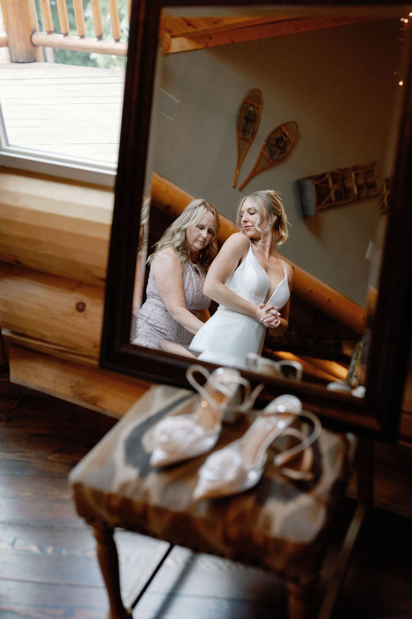 reflection in the mirror of the brides mother helps her put her wedding dress on