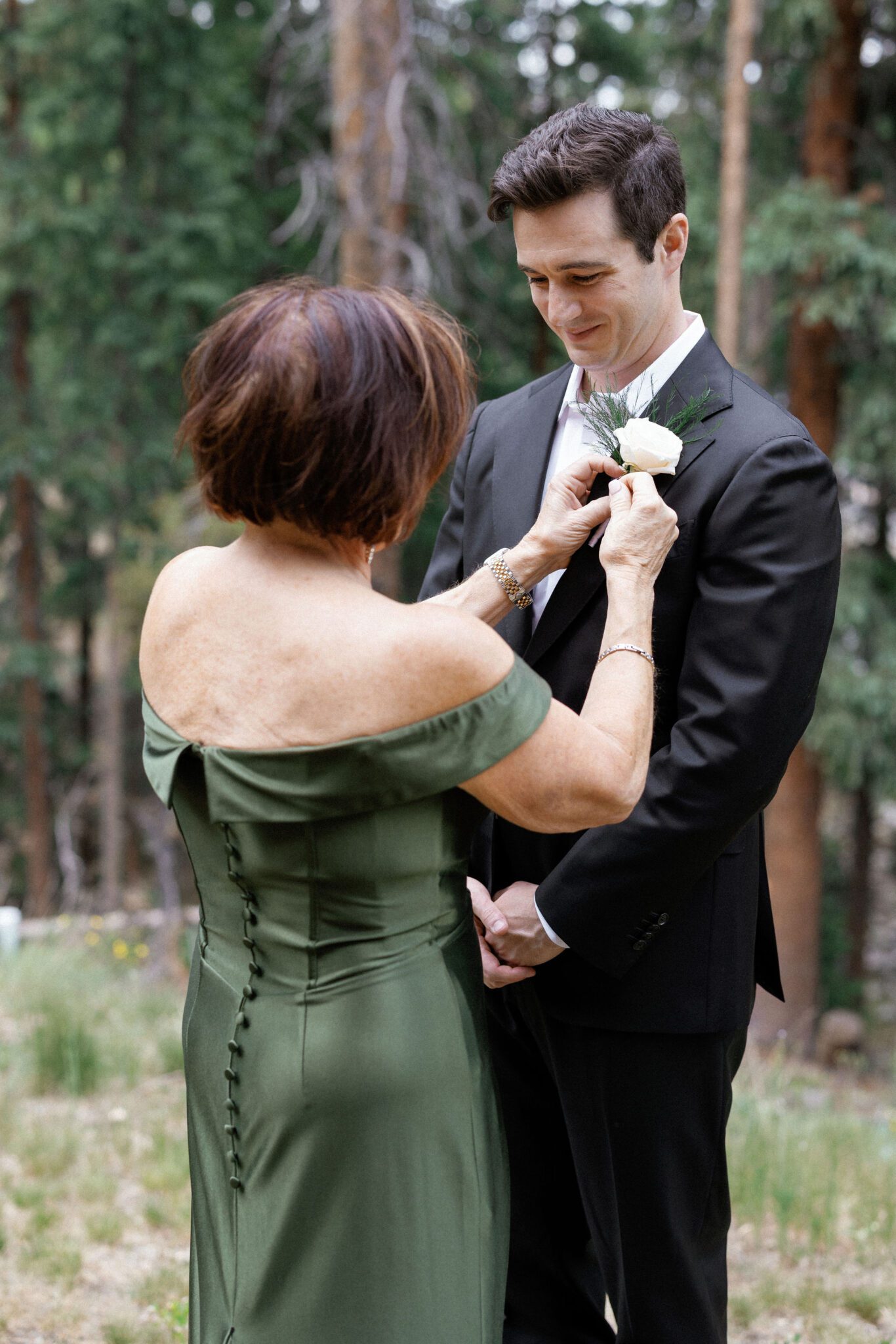 mother of the groom puts a boutonniere on the groom